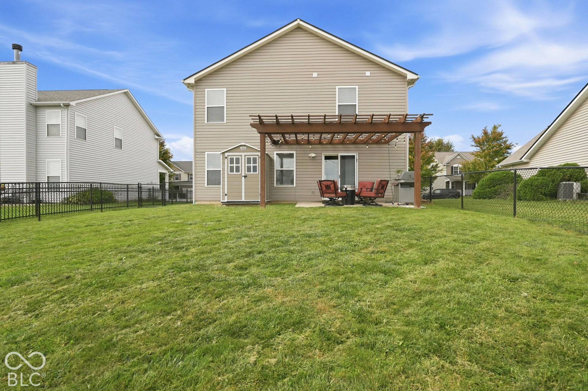 Expansive grassy yard featuring a chain-link fence, concrete patio, and a wood pergola