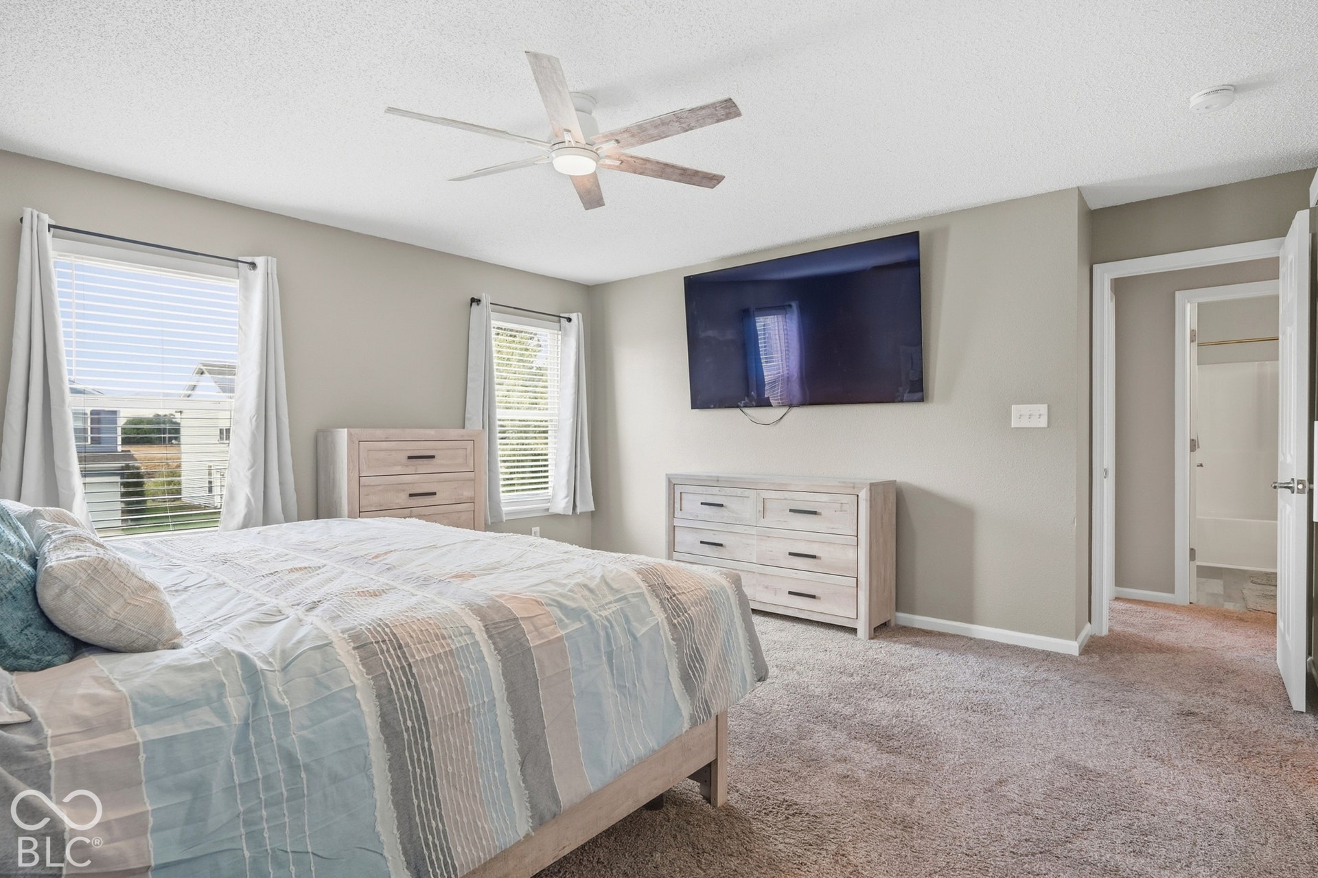 Carpeted bedroom featuring a ceiling fan, two windows with blinds, and neutral wall tones