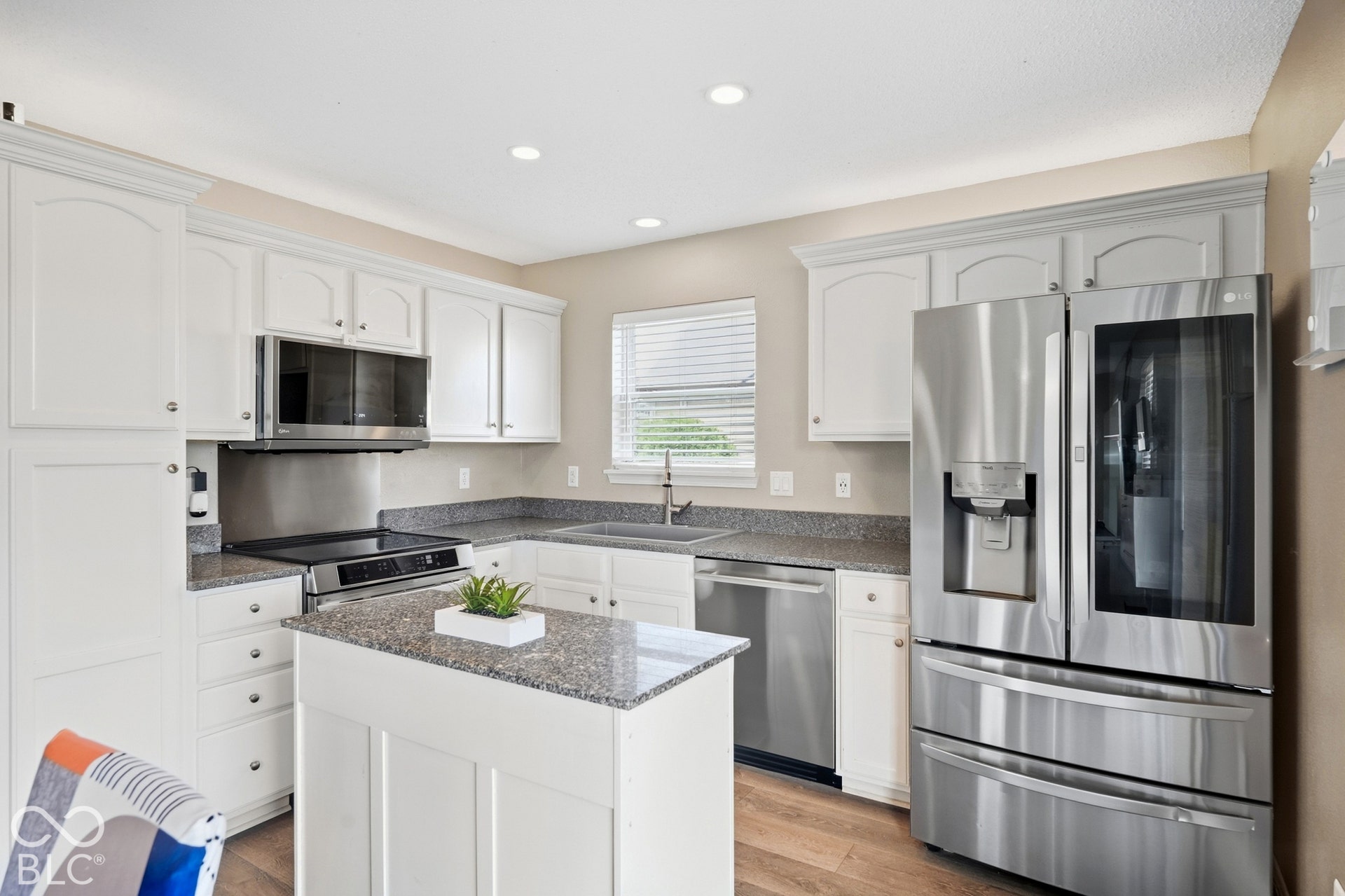Kitchen featuring white cabinetry, quartz countertops, stainless steel appliances, a center island, and wood-finish flooring