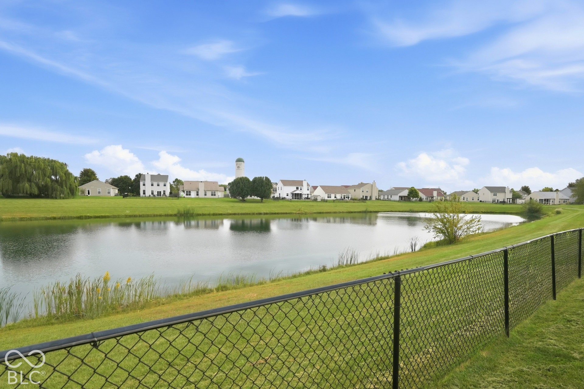 Chain-link fencing bordering a body of water with a grassy bank