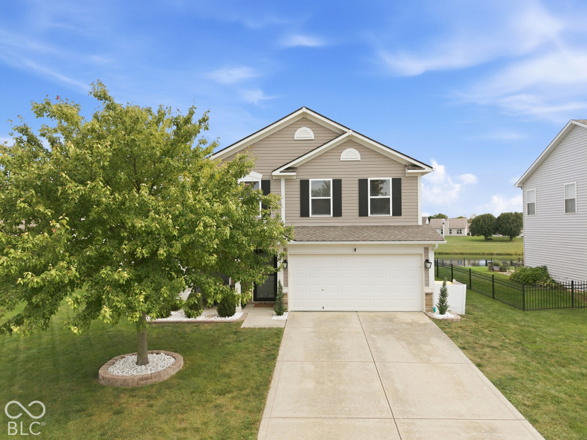 Two-story residence with a two-car garage, concrete driveway, and a front lawn with mature tree