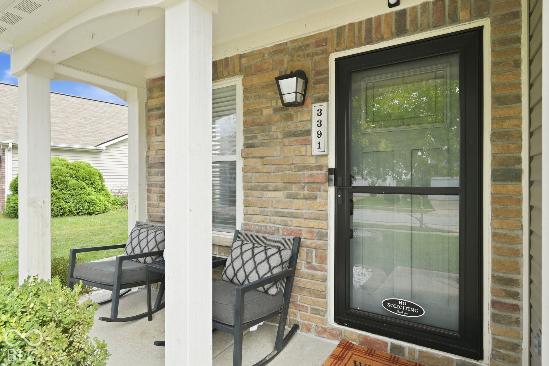Covered front porch featuring brick siding, white columns, and a black storm door