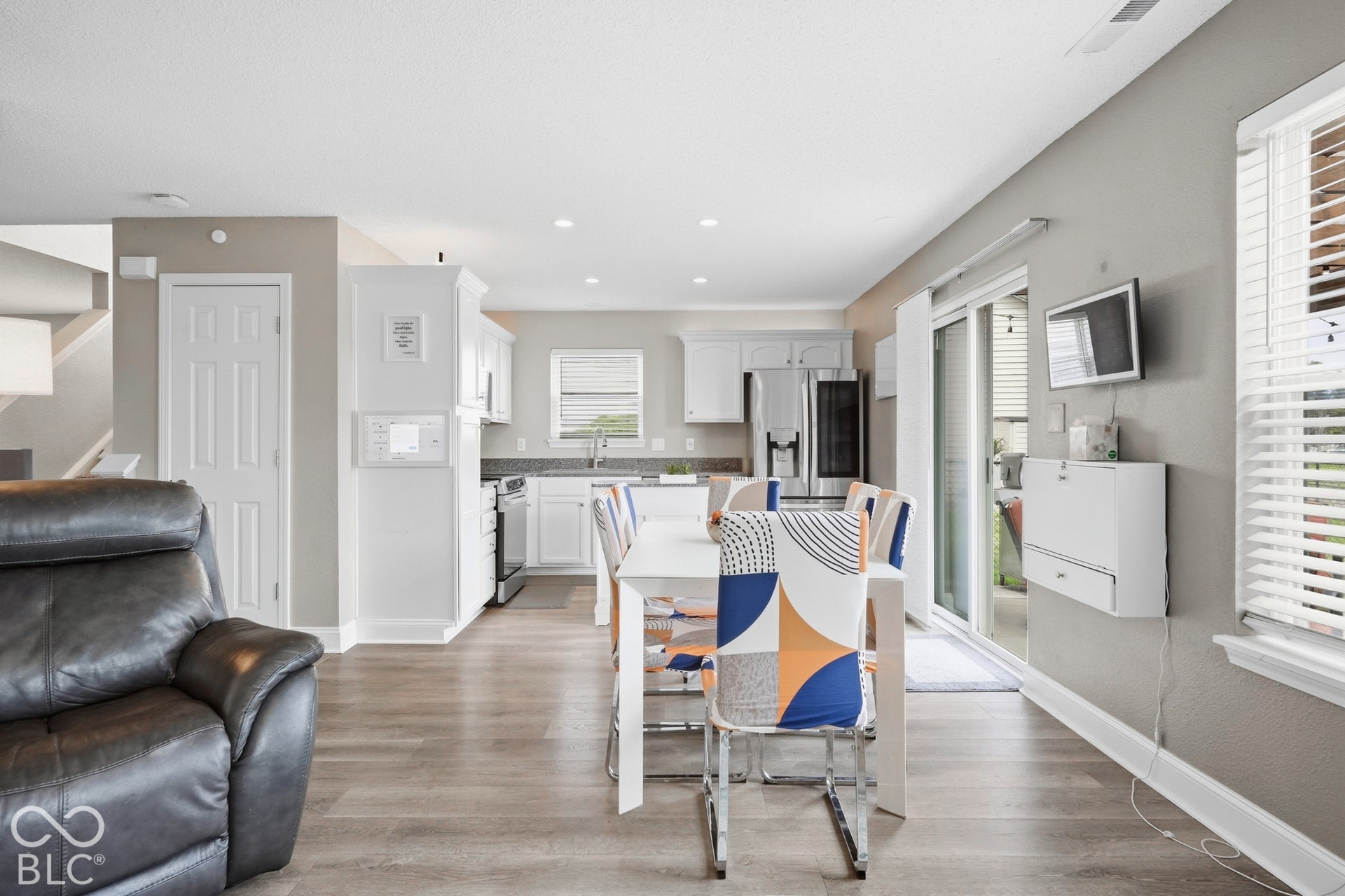Open-concept living space with wood-finish flooring, white cabinetry, stainless steel appliances, and sliding glass doors