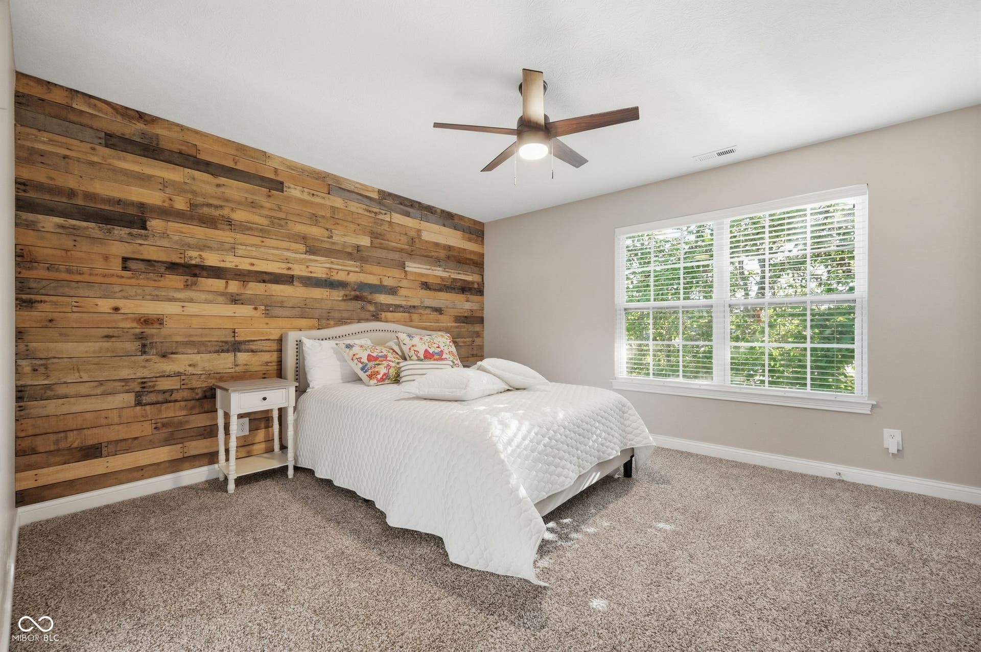 2743 Rylee Court, Greenwood, IN 46143 Wood-plank accent wall, broad window with multiple panes, textured carpeting, and a ceiling fan with integrated lighting