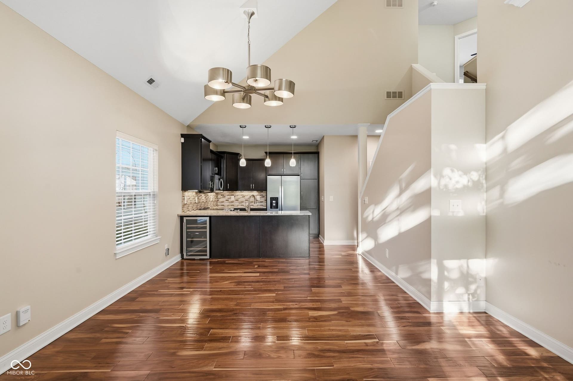 2743 Rylee Court, Greenwood, IN 46143 Vaulted ceiling with a contemporary chandelier, rich acacia hardwood flooring, dark wood cabinetry, stainless steel appliances, and a built-in beverage cooler
