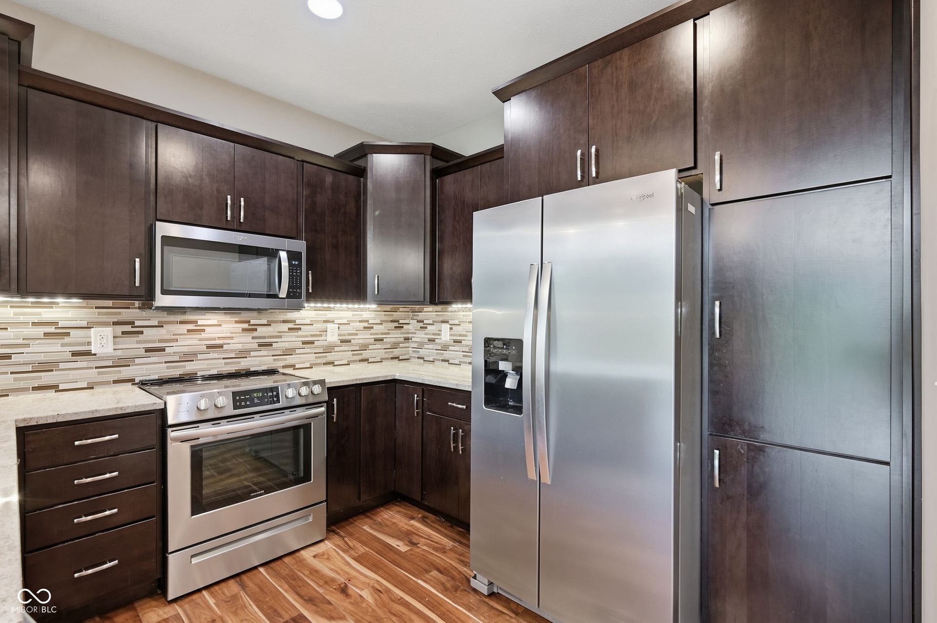 2743 Rylee Court, Greenwood, IN 46143 Kitchen featuring wood-finish flooring, dark wood cabinetry, stainless steel appliances, light-toned granite countertops, and a mosaic tile backsplash