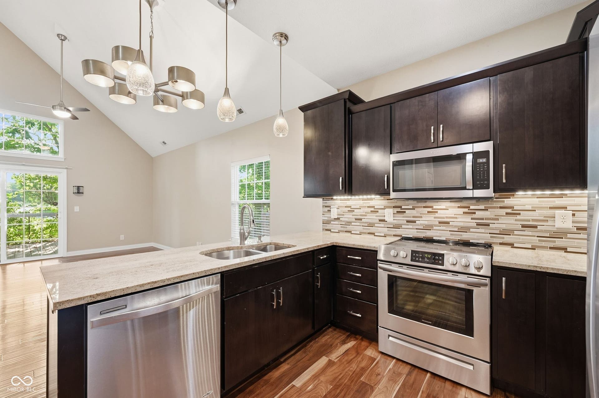 2743 Rylee Court, Greenwood, IN 46143 Vaulted ceiling with modern lighting fixtures, wood-finish flooring, stainless steel appliances, granite countertops, and a tiled backsplash