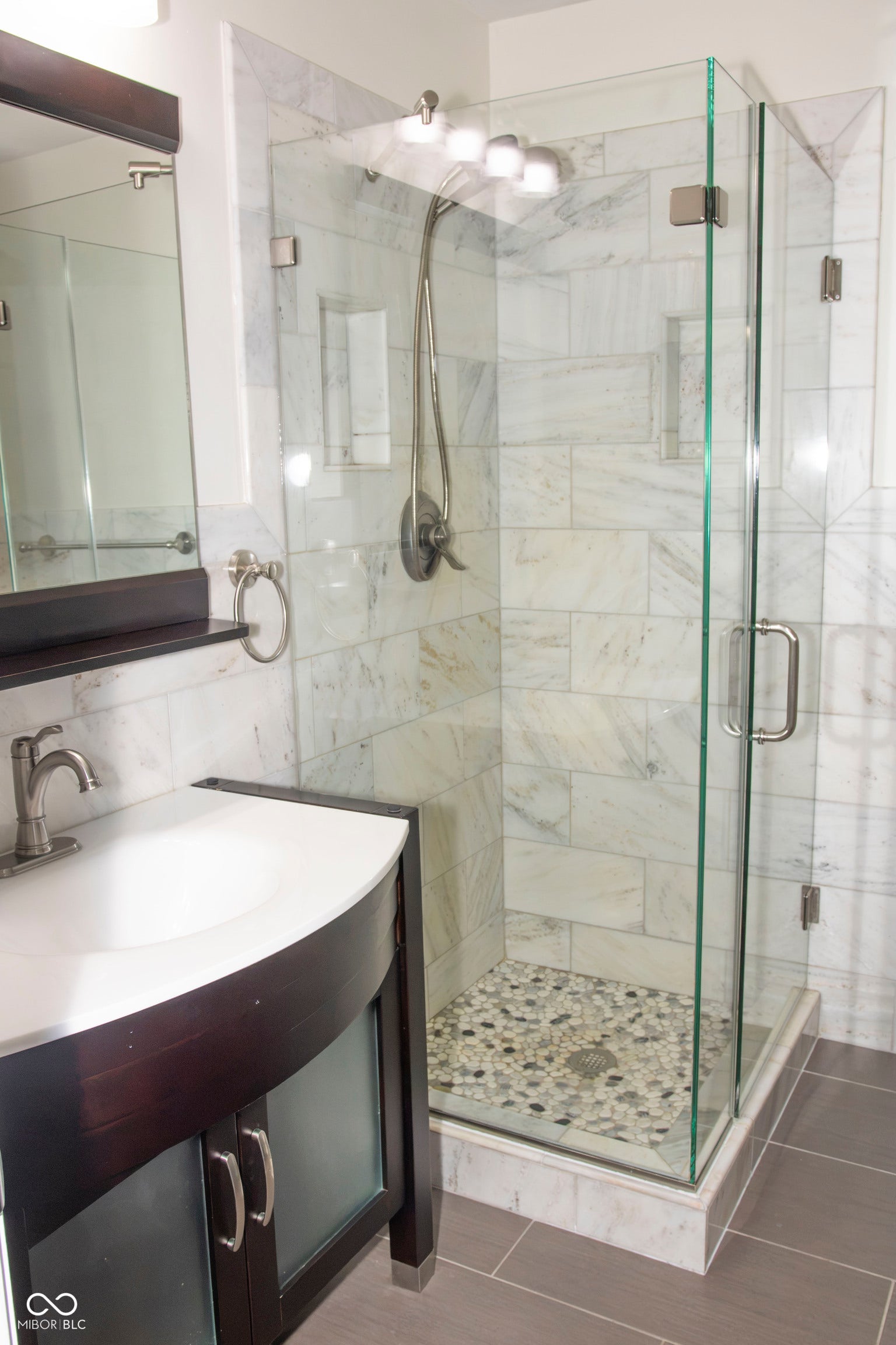 Walk-in shower with clear glass enclosure, natural stone tile surround, and pebble-finish shower pan