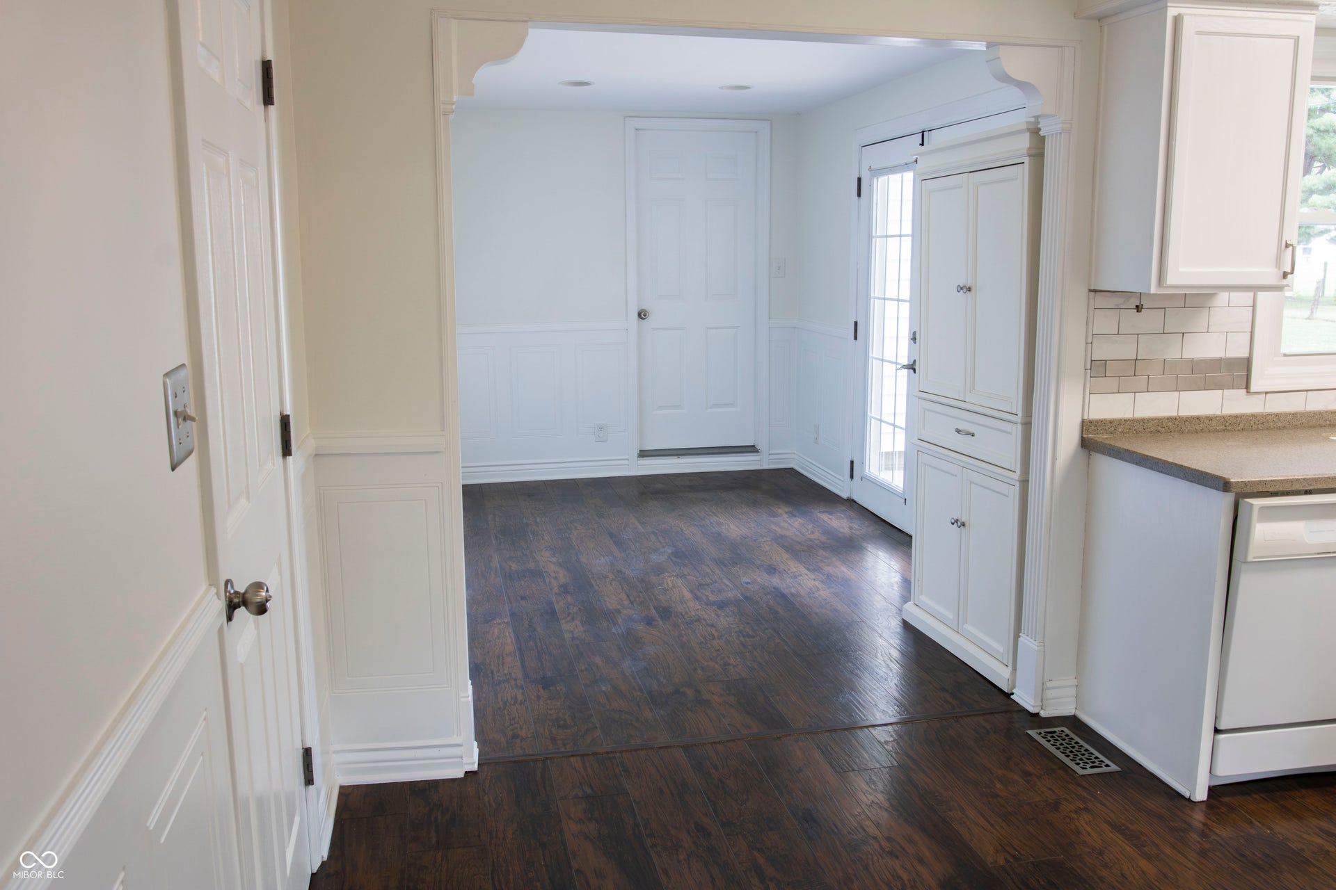 Wood-finish flooring throughout, white wainscoting, white cabinetry, and a tile backsplash