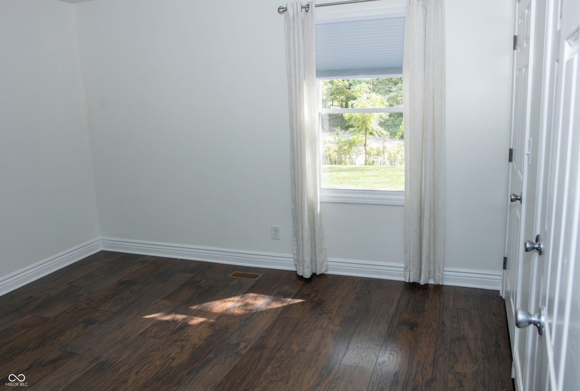 Wood-finish flooring, white walls, and a window with a roller shade