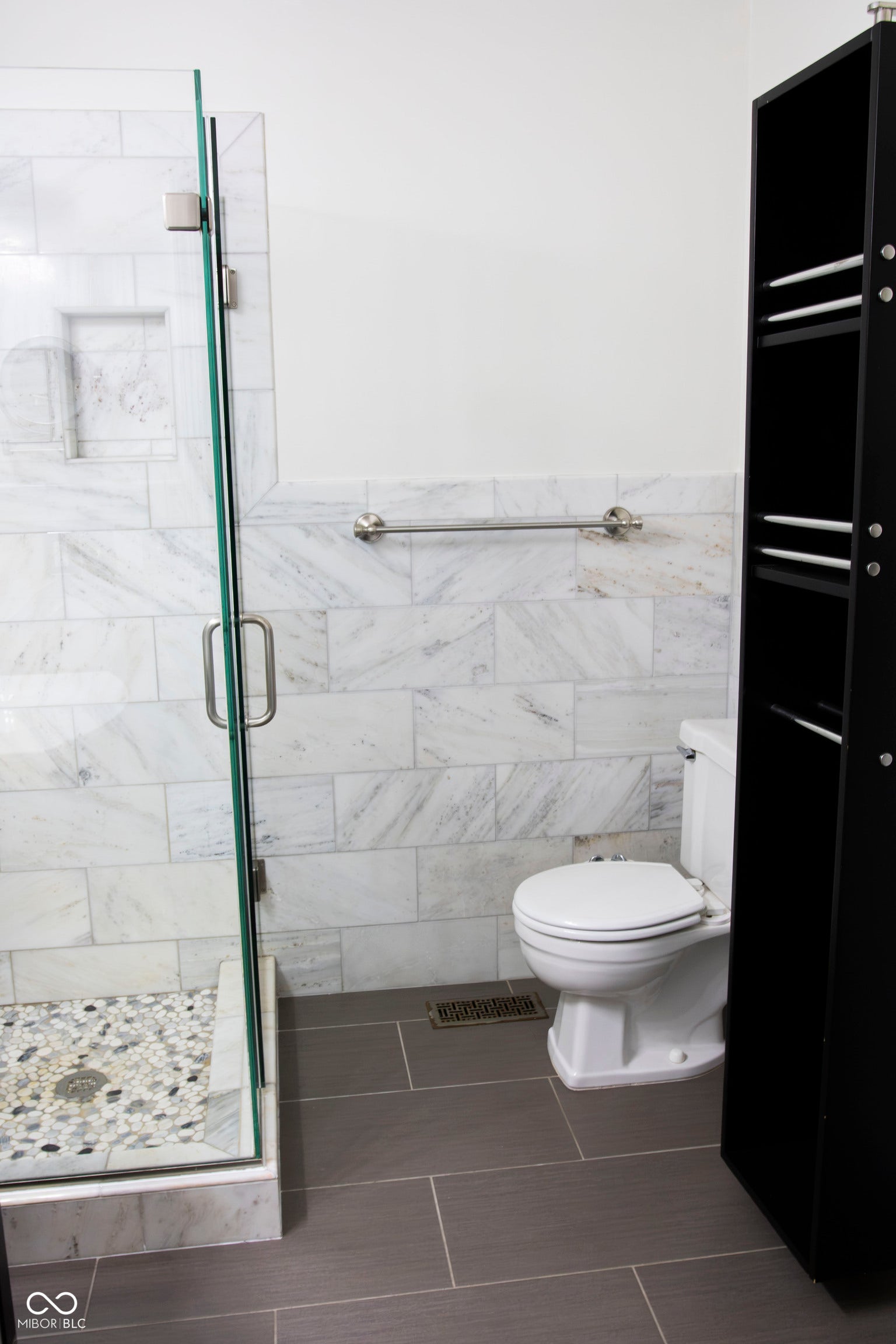 Glass-enclosed shower with a recessed niche, pebble-tiled shower floor, and stone tile walls