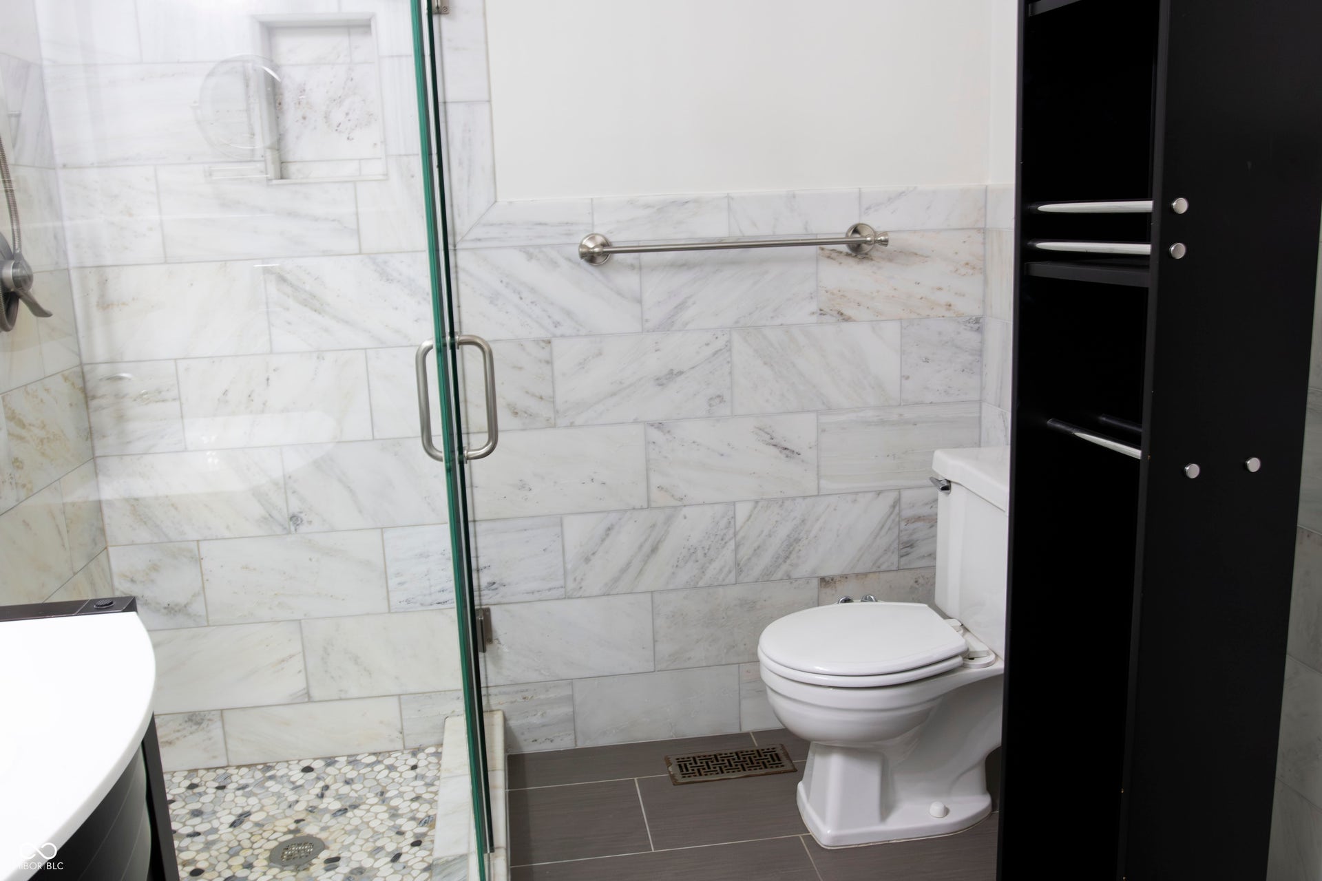 Glass-enclosed shower with a tiled surround, recessed shower niche, and pebble-finish floor