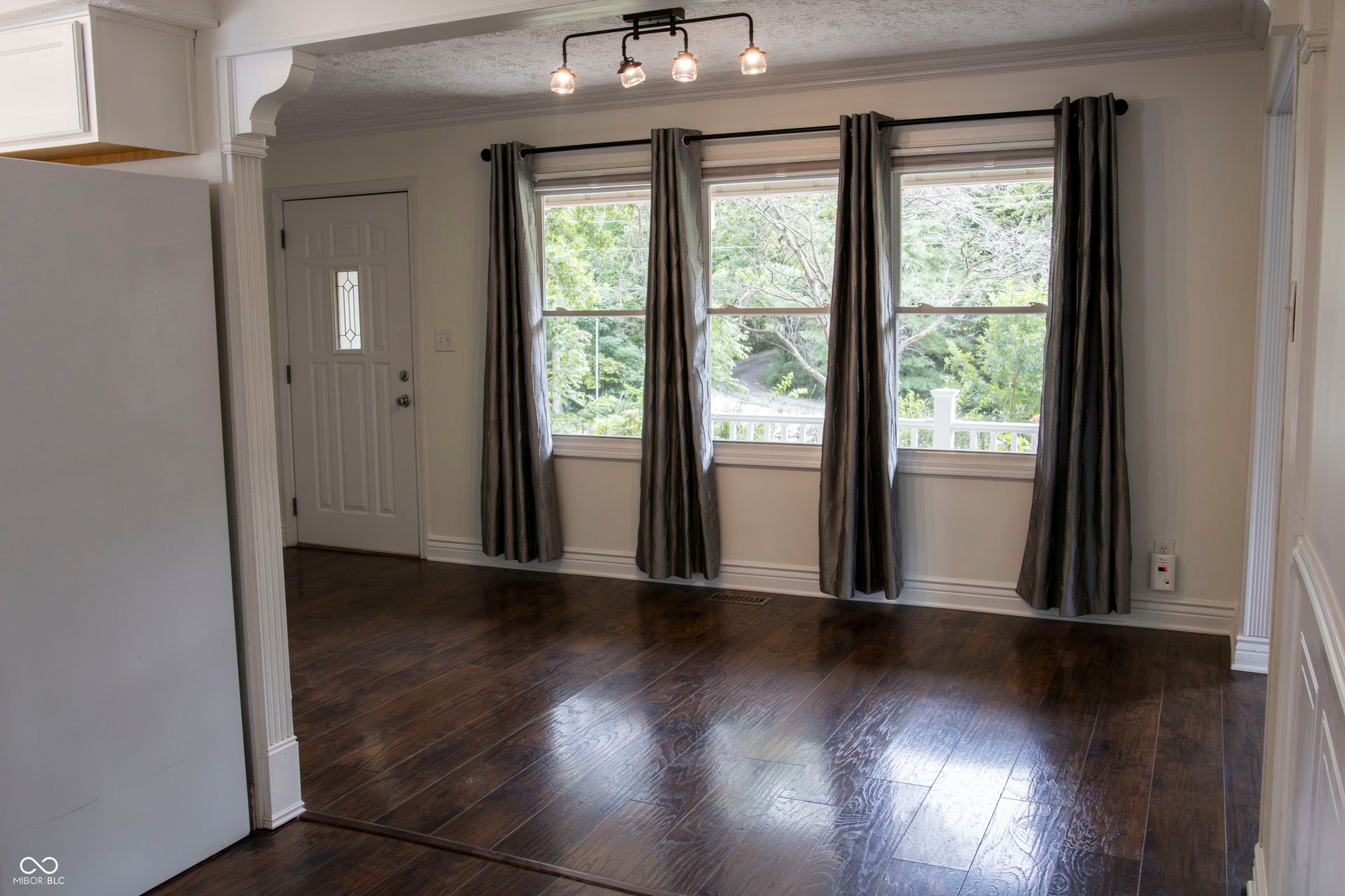 Hardwood flooring, three large windows, white trim, decorative archway, and a contemporary track light fixture