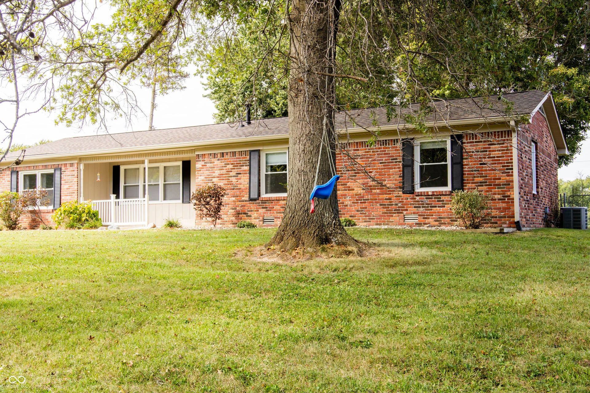 Brick exterior with dark shutters, covered front porch with white railing, and a dark shingle roof