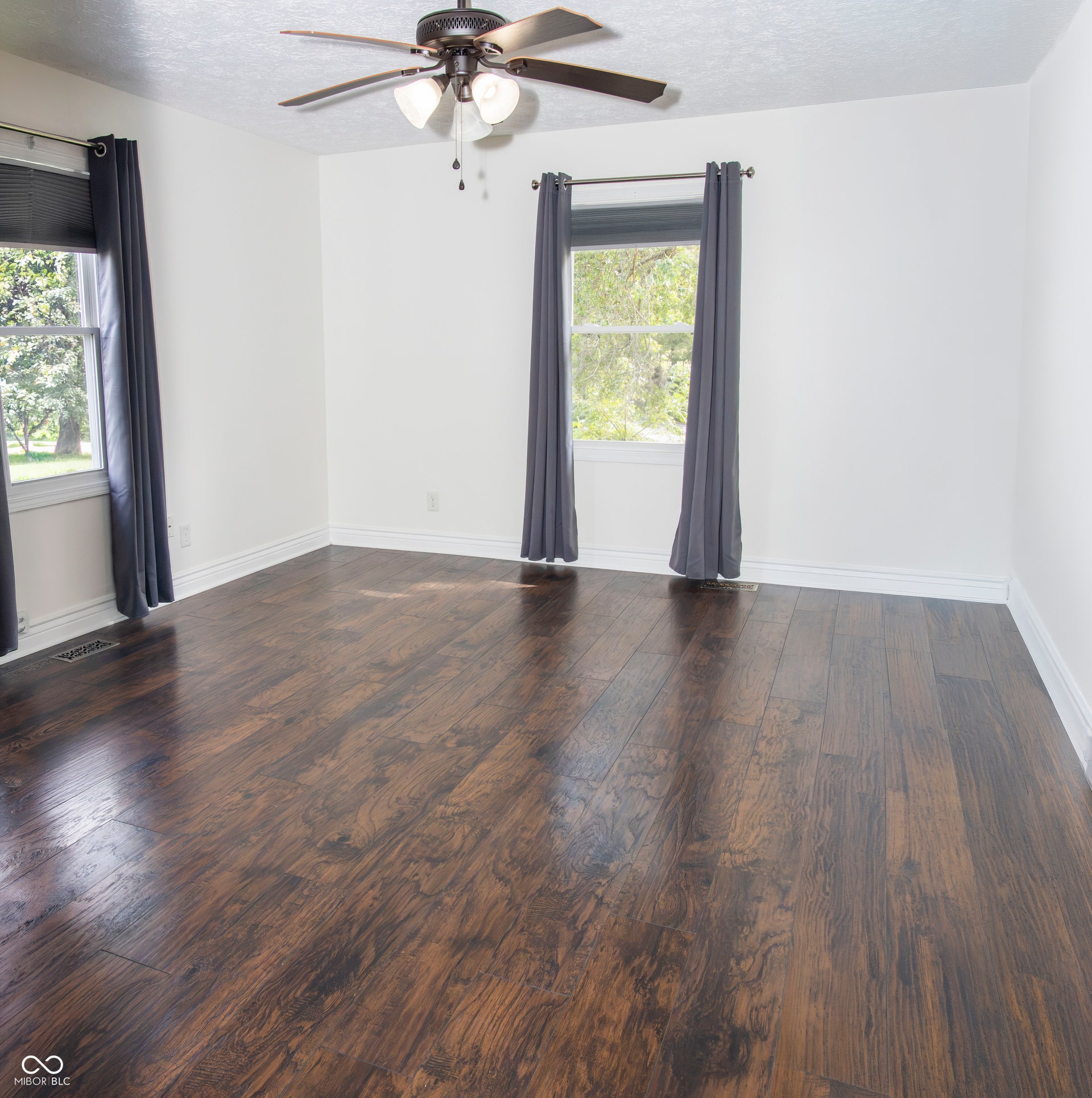 Spacious room featuring wood-finish flooring, white walls, and a ceiling fan with integrated lighting