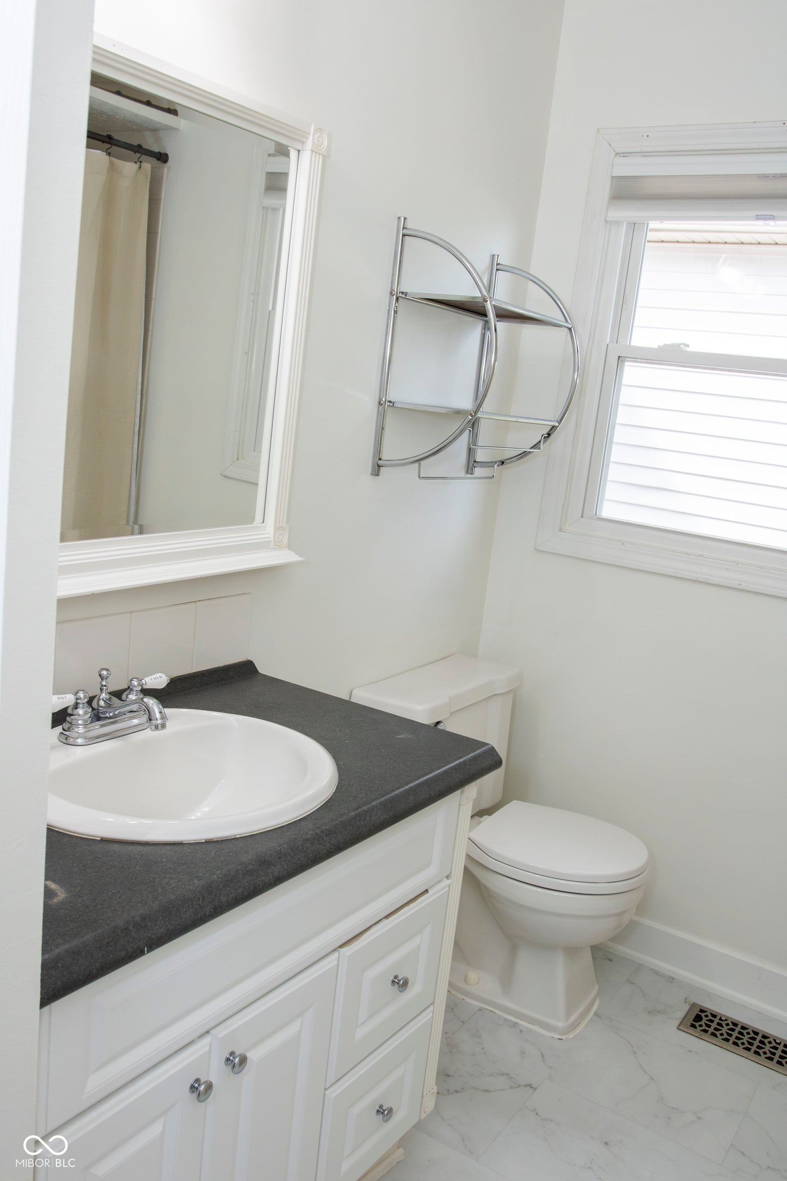 White vanity with chrome hardware, dark countertop, built-in sink, and framed mirror