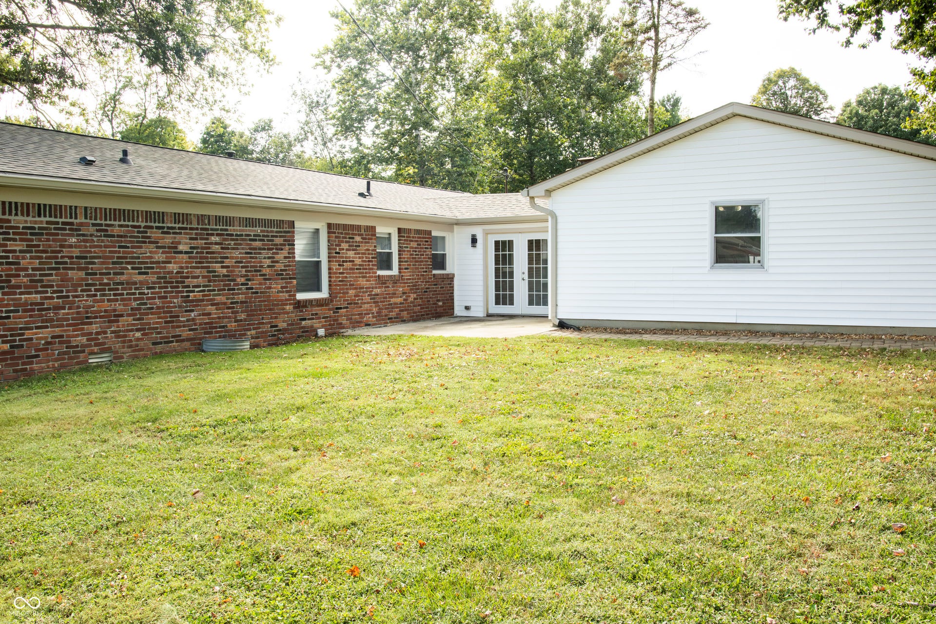 Expansive lawn with mature trees, brick exterior, white siding, and double French doors opening to a concrete patio