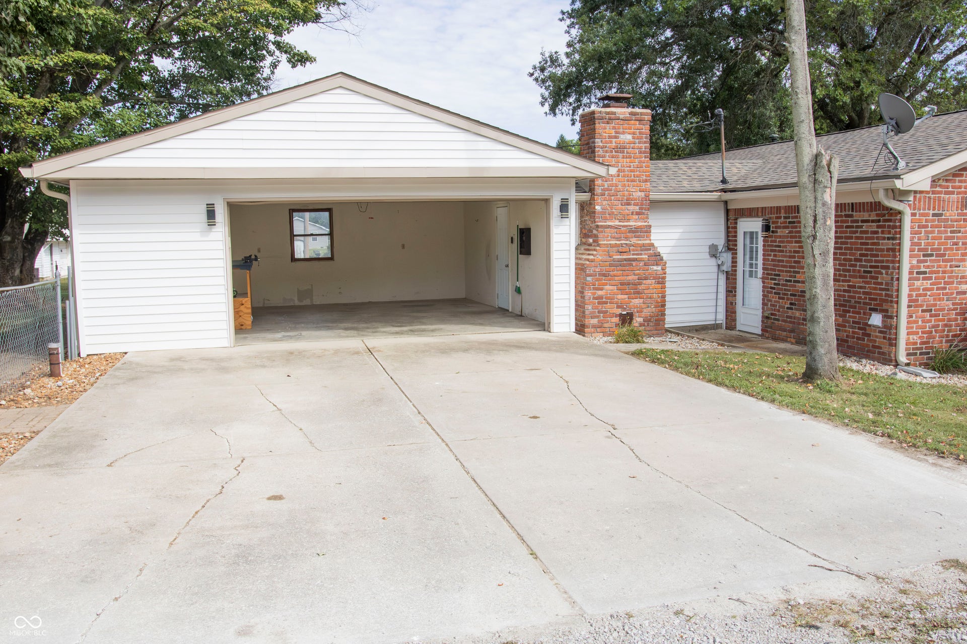Attached two-car garage with white siding, concrete driveway, brick chimney, and a side entry door