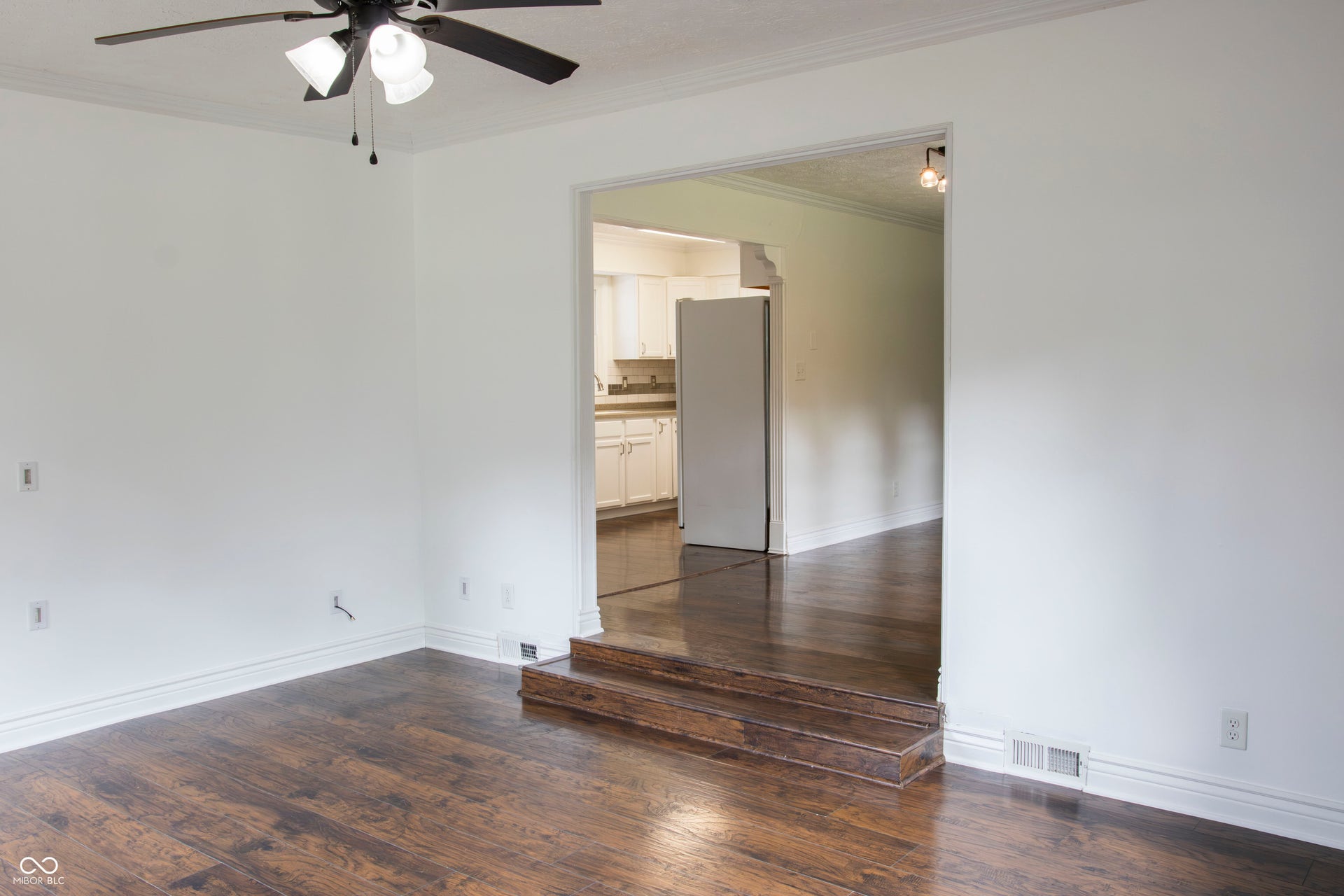 Wood-finish flooring with white baseboards, crown molding, and a ceiling fan with integrated lighting