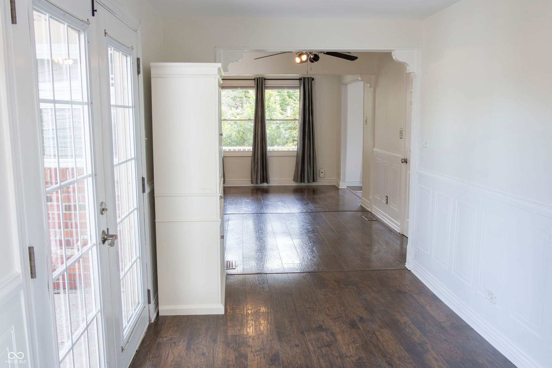 French doors with glass panels, dark wood-finish flooring, white paneled wainscoting, and an arched entryway