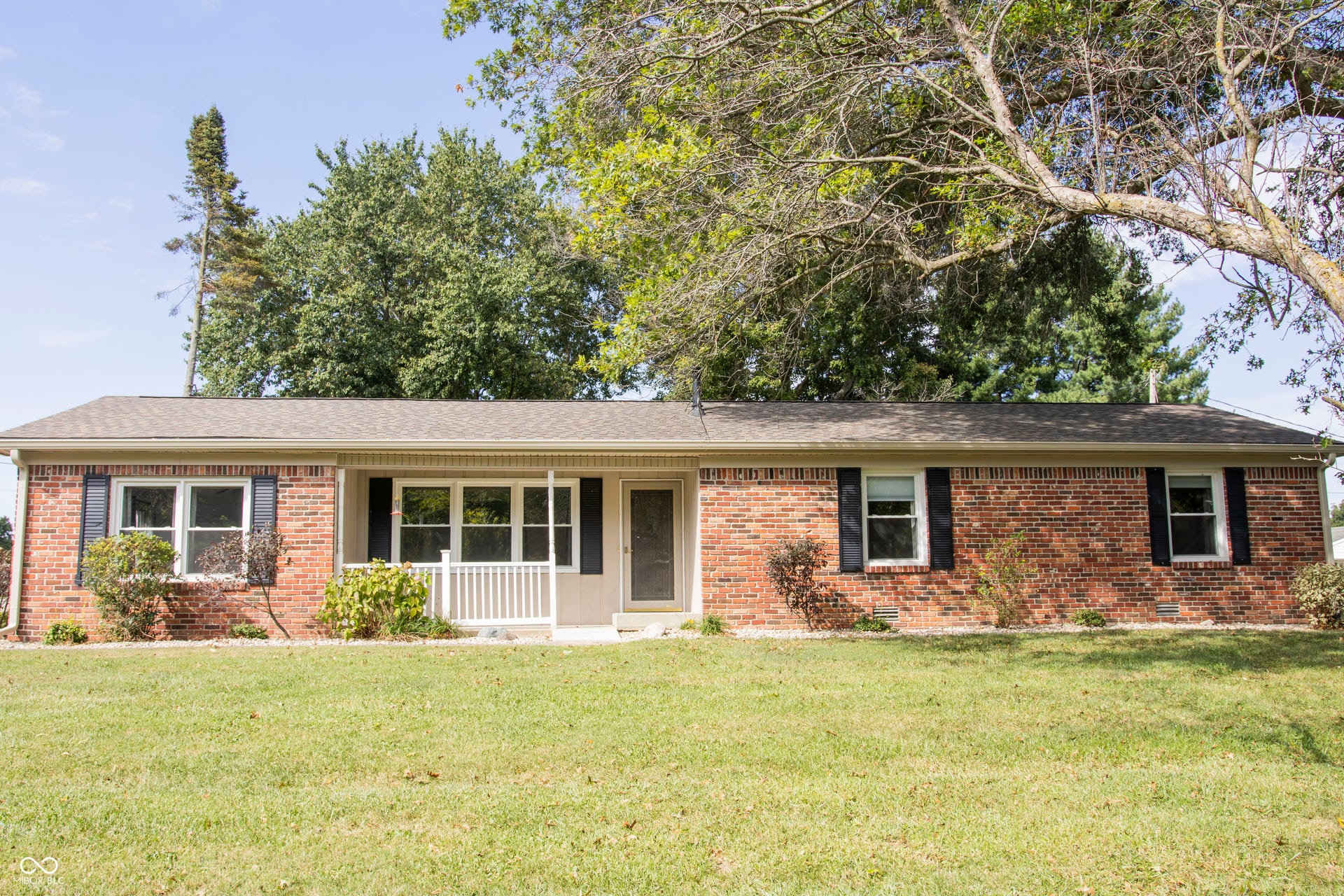Brick exterior with dark shutters, covered front entry, and a pitched shingle roof