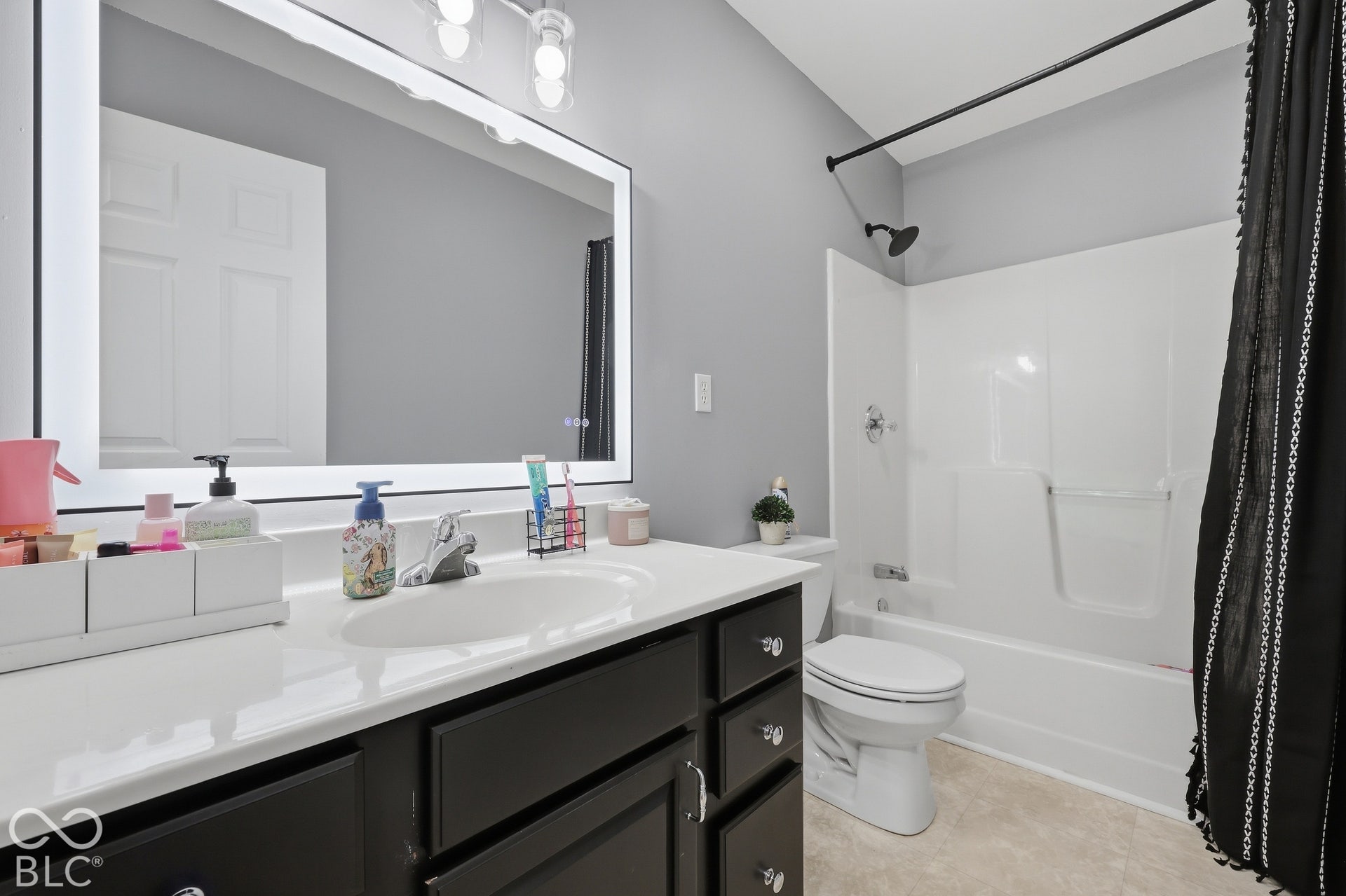 6x10 upstairs full bath features a spacious vanity with dark-cabinetry, a large lighted mirror, and a shower and tub combo.