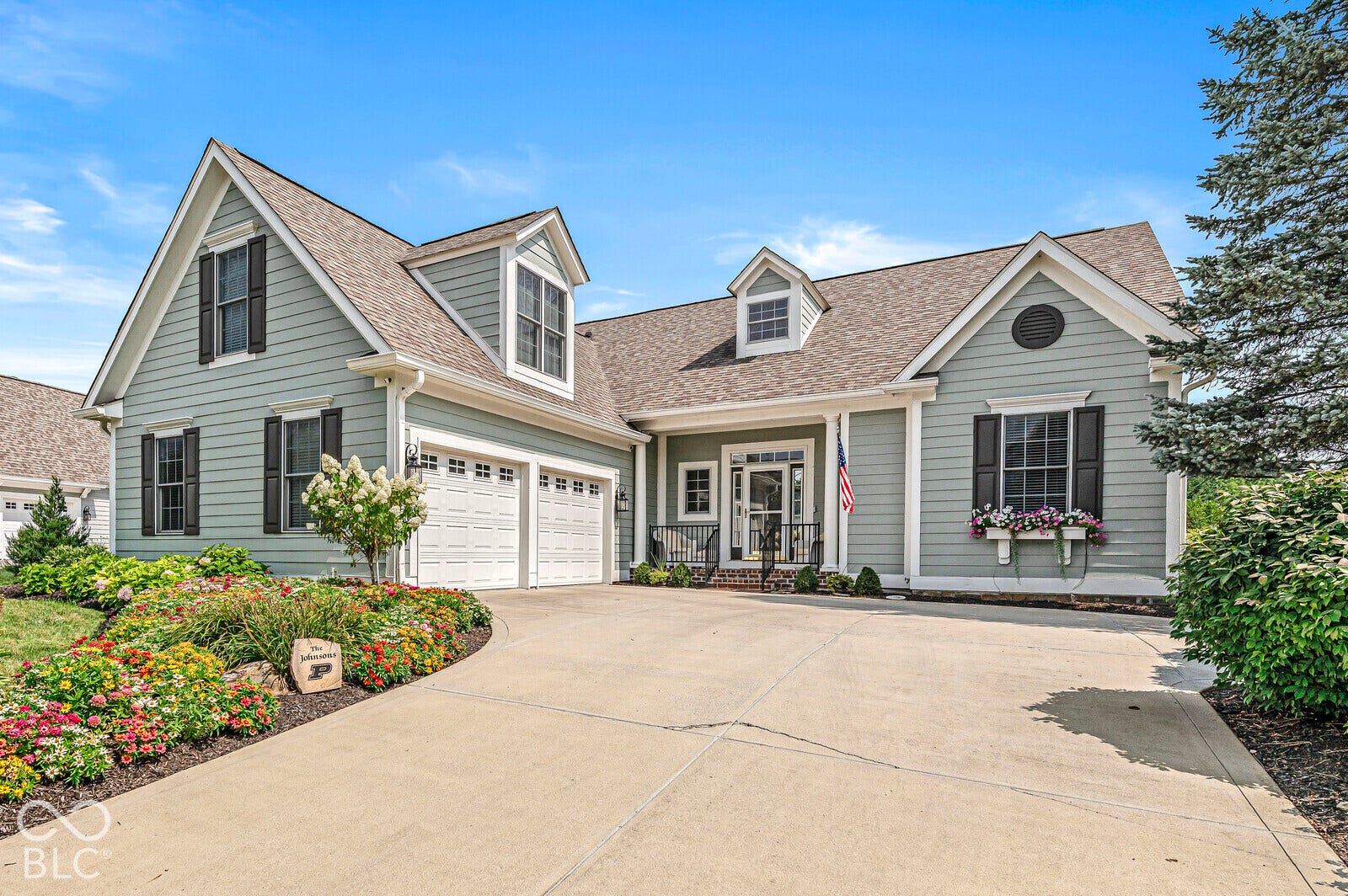 Two-car garage with white paneled doors, light green siding with white trim, dormer windows, and a concrete driveway