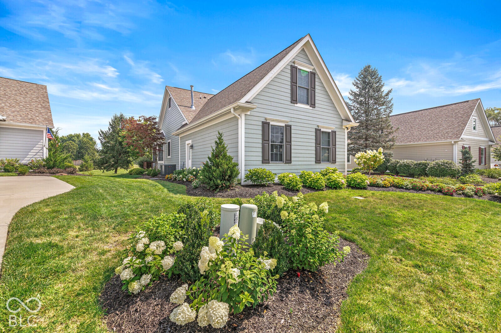 Gabled roofline, light-colored siding, dark window shutters, established landscaping, and a manicured lawn