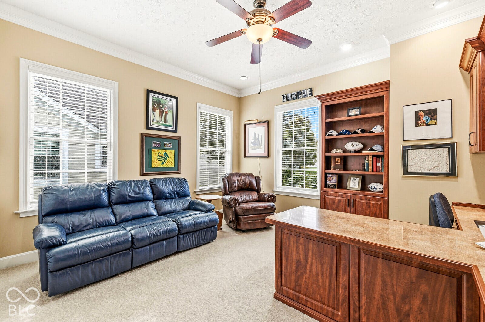 Built-in shelving, crown molding, a ceiling fan with integrated lighting, recessed lighting, and multiple windows with blinds