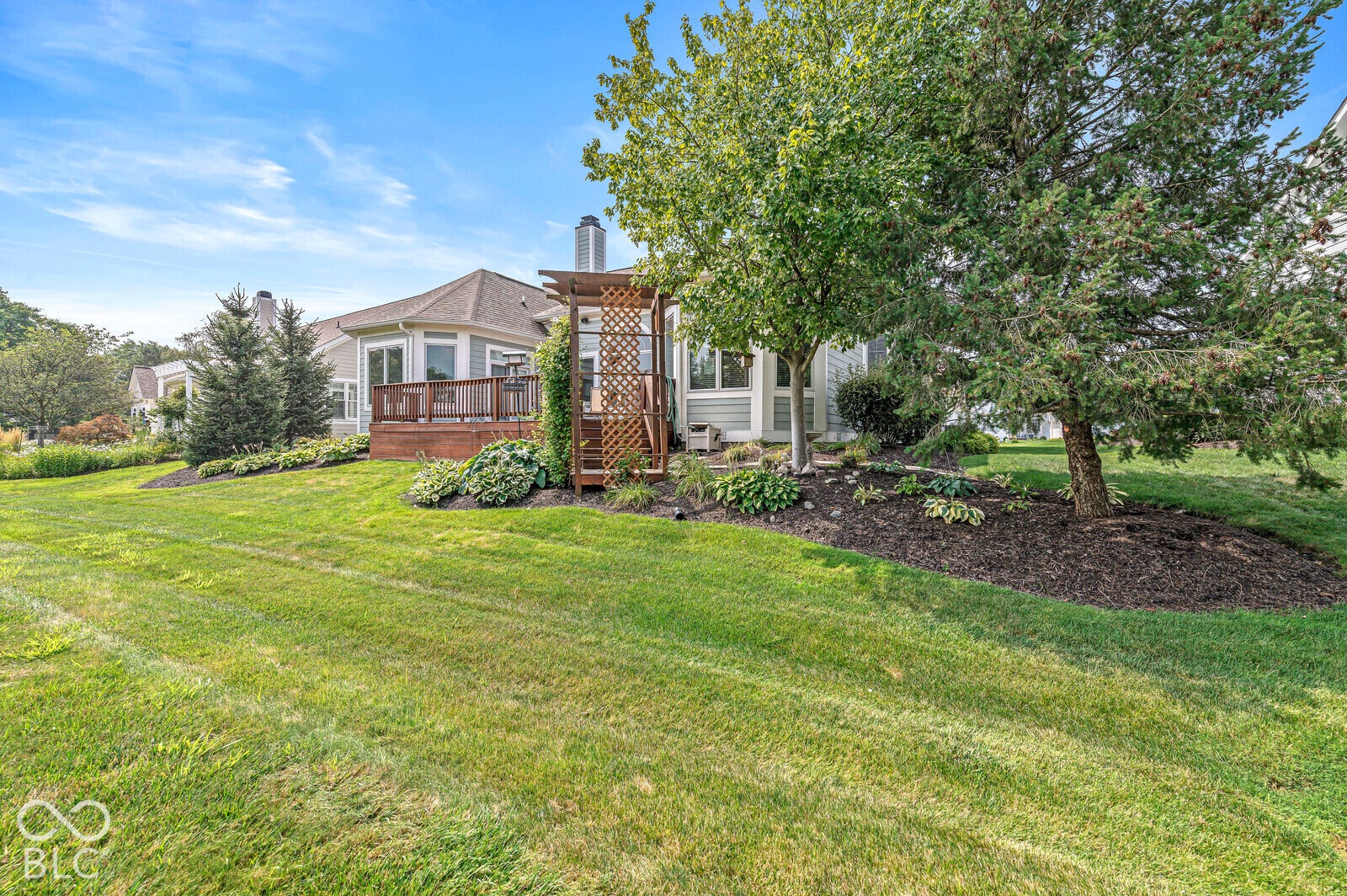 Spacious backyard featuring a sloped lawn, mature trees, and landscaping beds