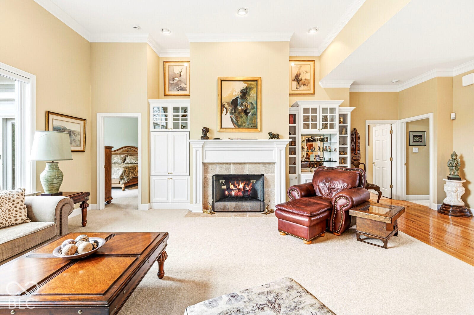 Spacious living area featuring a fireplace with stone surround, custom built-in cabinetry, crown molding, and recessed lighting