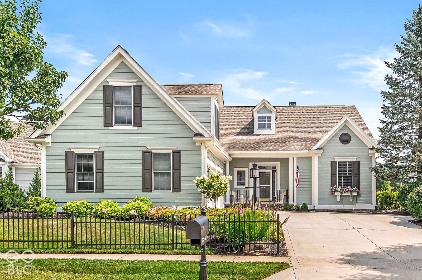 Gabled architectural elements, light-colored siding, dark window shutters, established landscaping, and a paved driveway