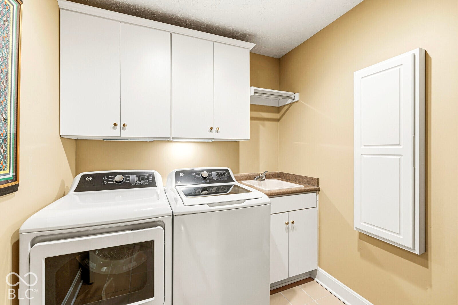 White upper cabinetry, under-cabinet lighting, integrated sink with brown countertop, white lower cabinetry, and tiled flooring