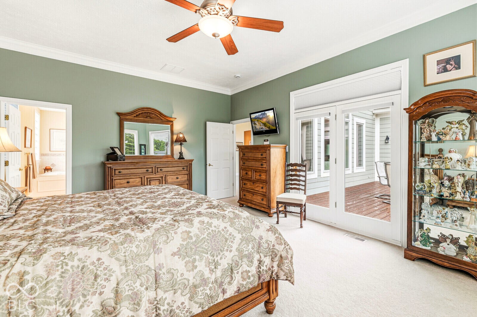White crown molding, ceiling fan with integrated lighting, light-colored carpeting, and double glass doors opening to an outdoor deck