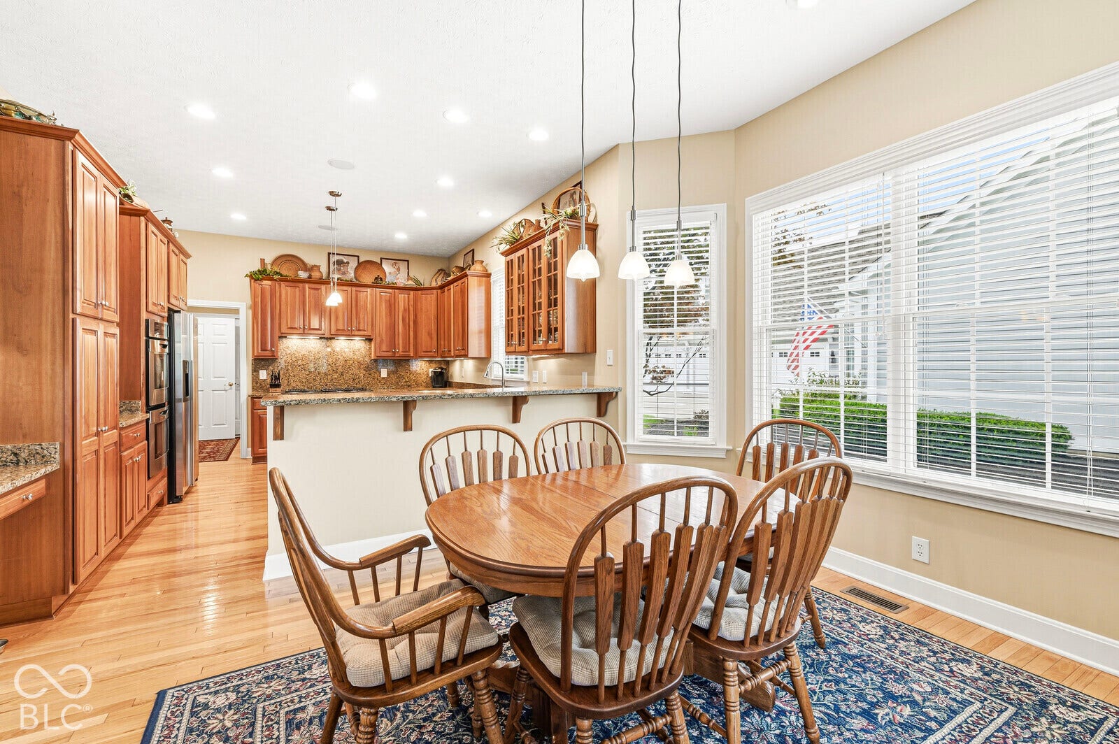Hardwood flooring, kitchen with wood cabinetry, integrated stainless steel appliances, granite countertops, and multiple windows