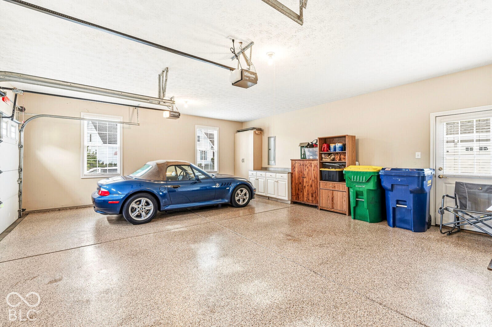 Two-car garage featuring an epoxy-coated concrete floor, two garage door openers, and built-in white cabinetry with a light-colored countertop