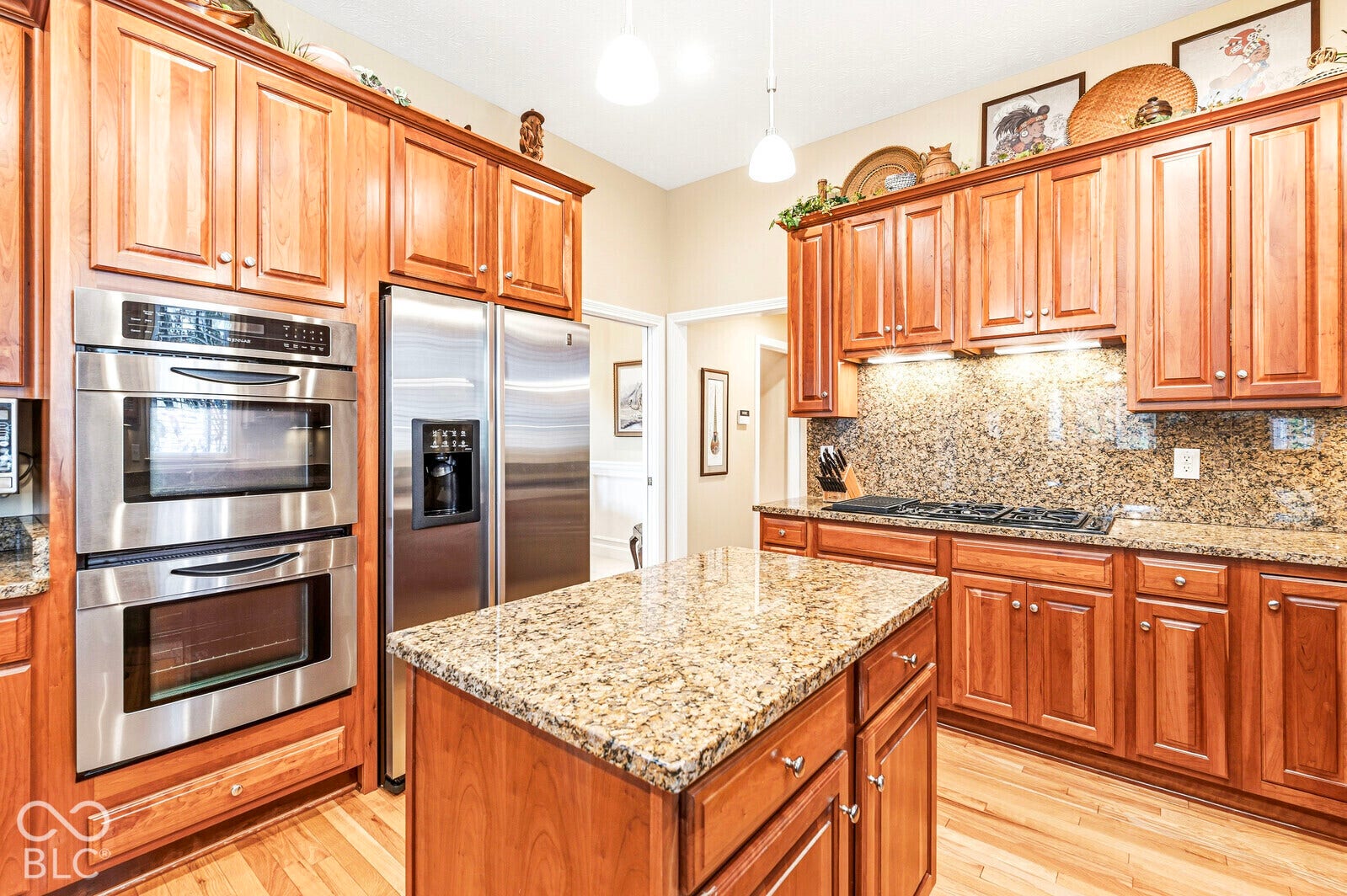 Kitchen featuring wood cabinetry, stainless steel double wall ovens, a stainless steel refrigerator, a center island with a stone countertop, and wood-finish flooring