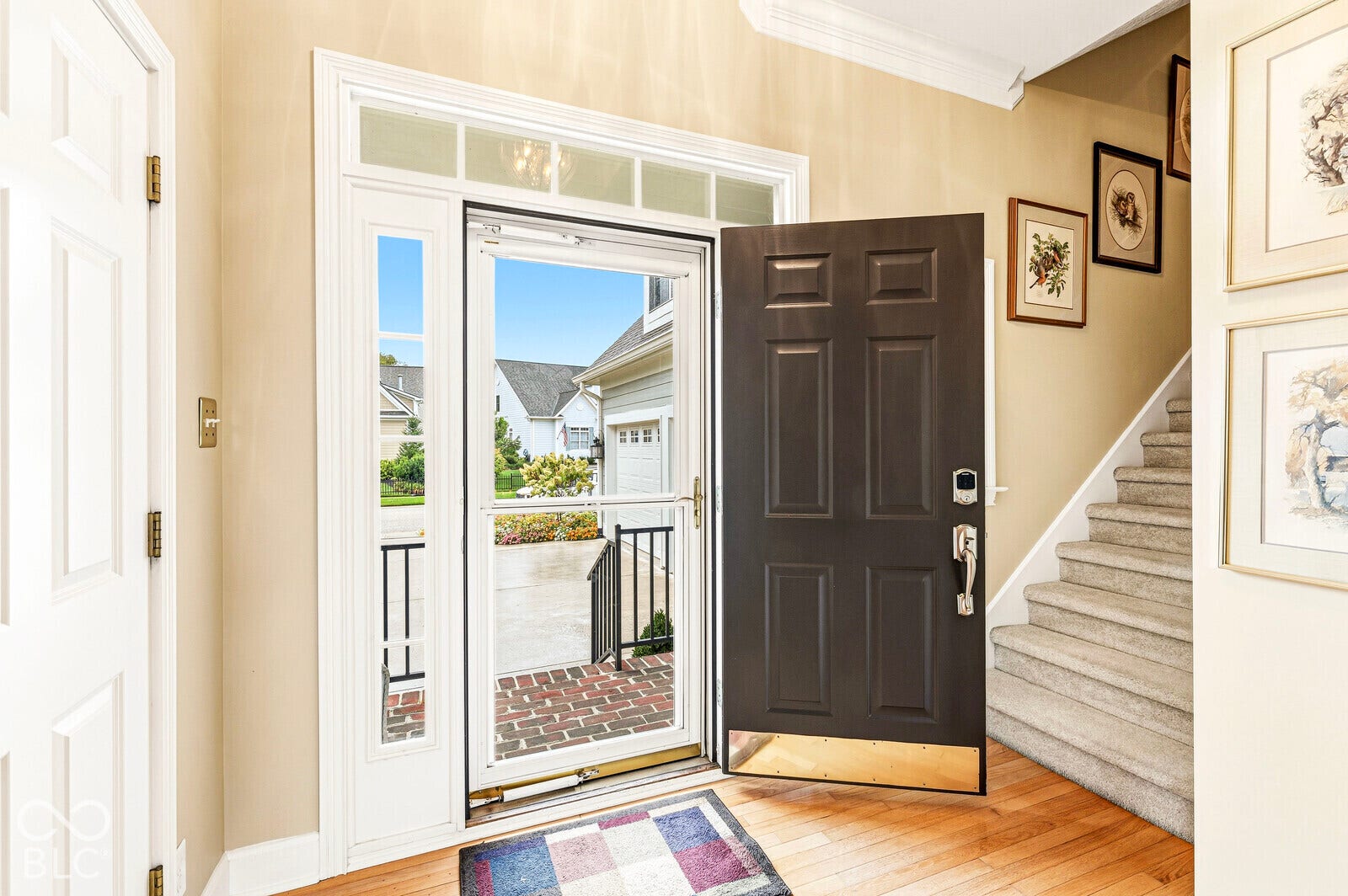 Hardwood flooring, paneled entry door, storm door, transom window, and carpeted staircase