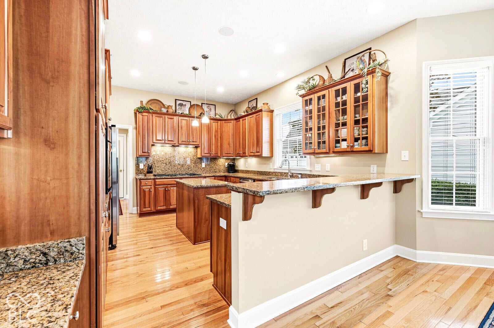 Hardwood flooring, wood-finish cabinetry, recessed lighting, stone countertops, and a kitchen island