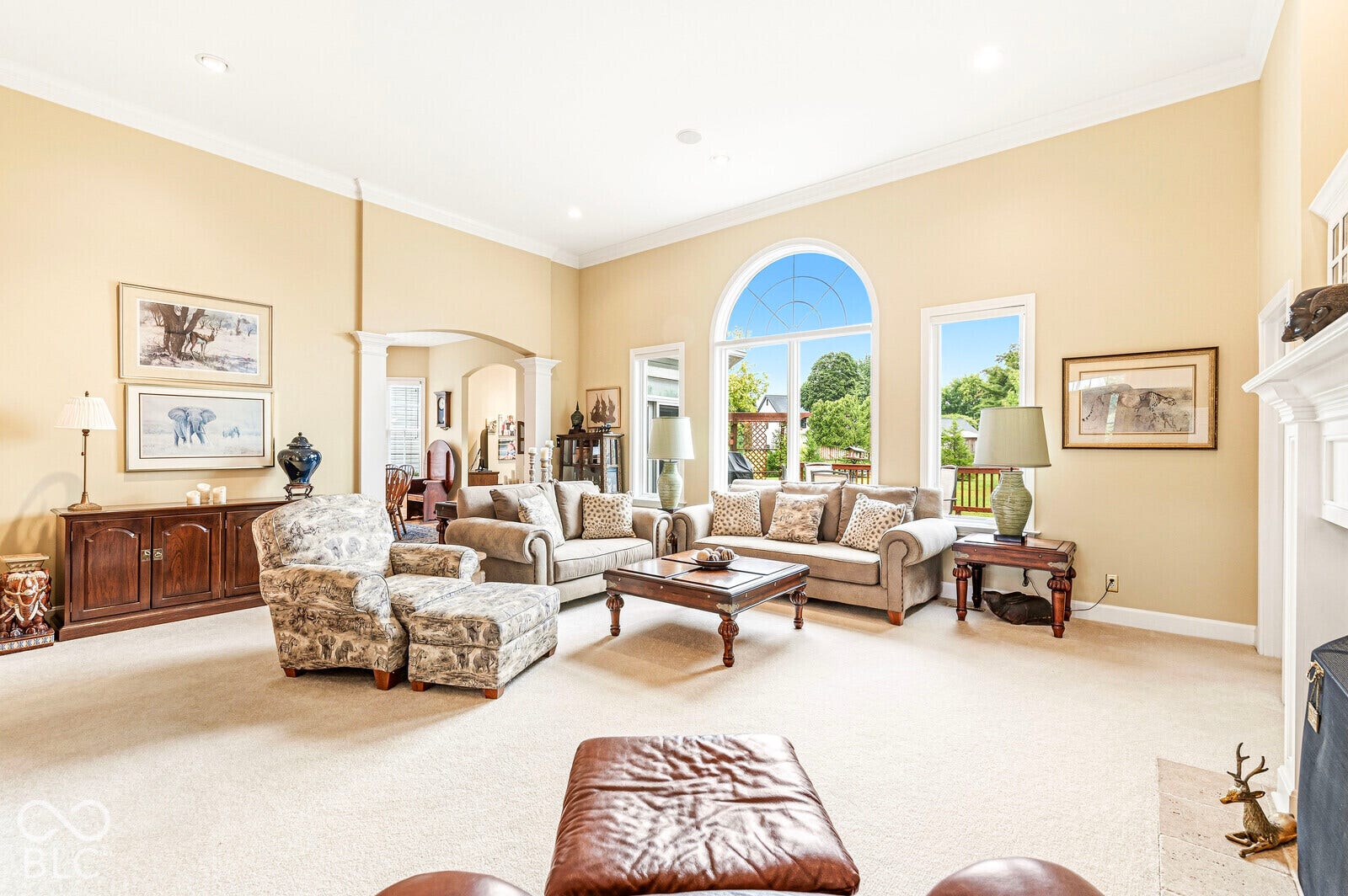 Vaulted ceiling with crown molding, arched entryway, and large windows with transom