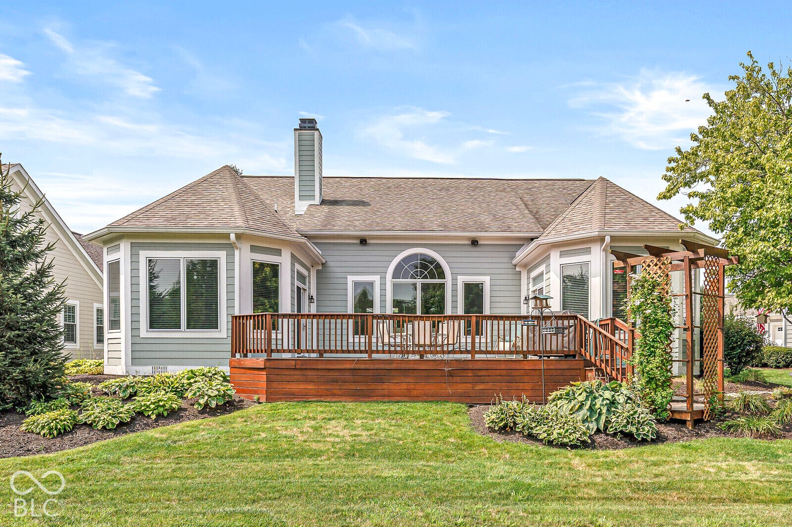 Expansive wood deck with railing, arched window, bay windows, and a pergola with lattice