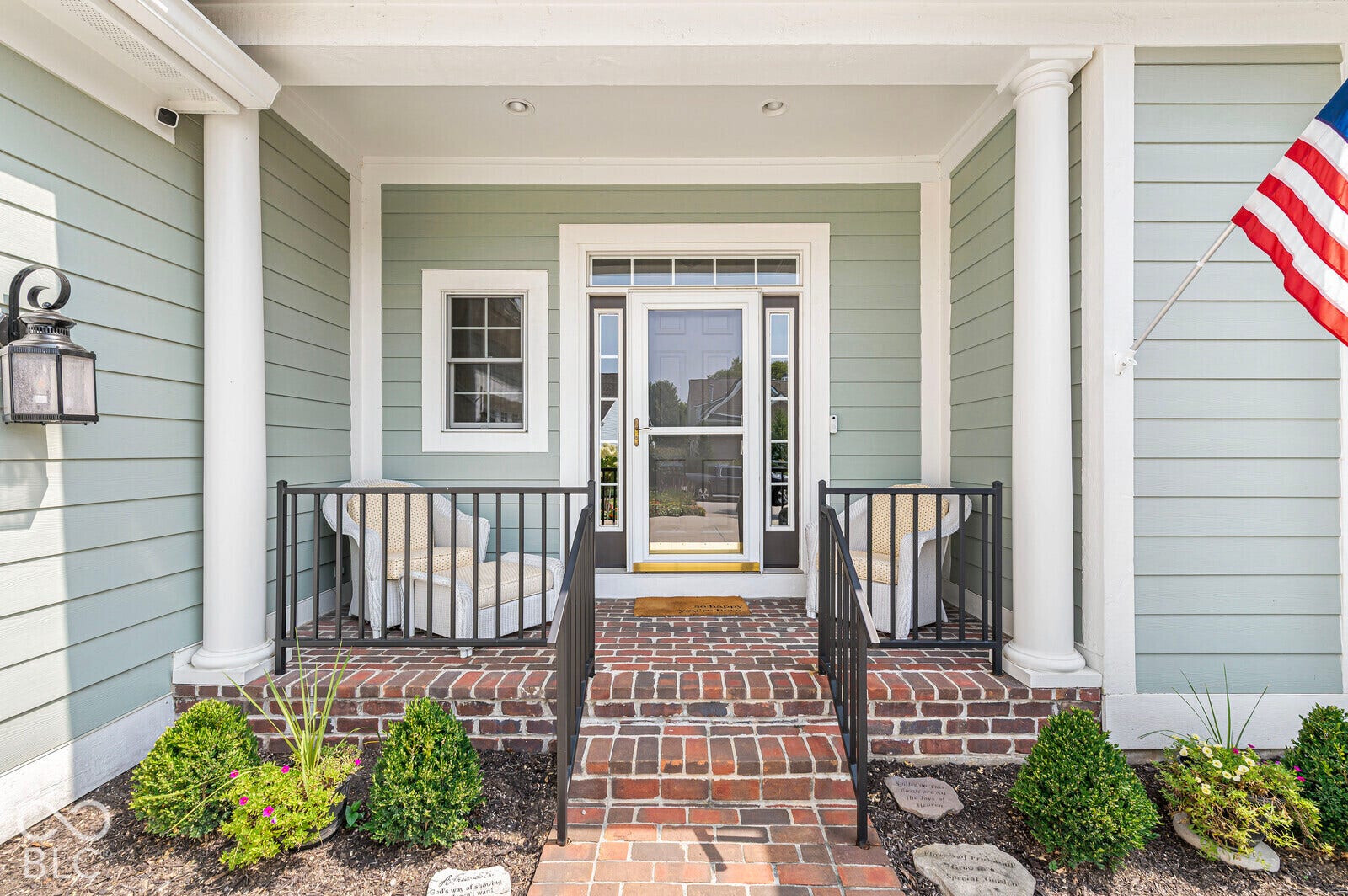 Front porch with brick steps and landing, white columns, decorative black railings, and a hanging lantern