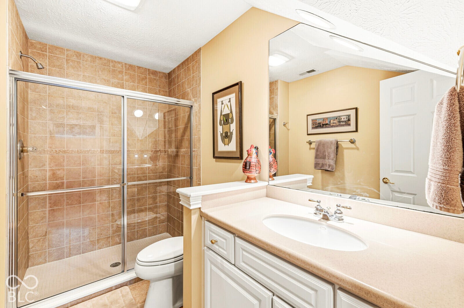 Shower with glass enclosure and tiled walls, white vanity with integrated sink, and full-width mirror