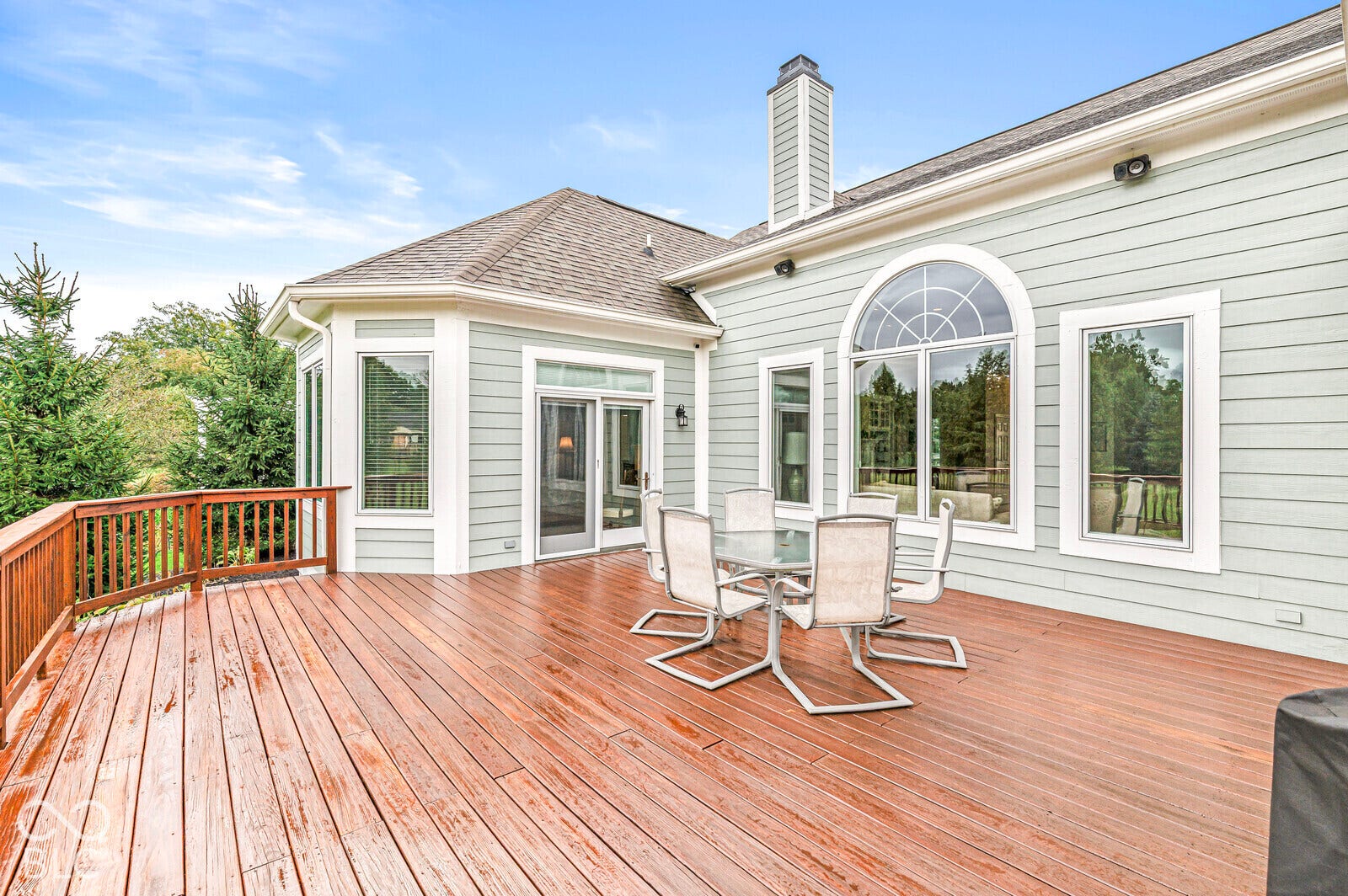 Expansive wood deck with a wood railing, siding exterior, large arched window, and sliding glass doors