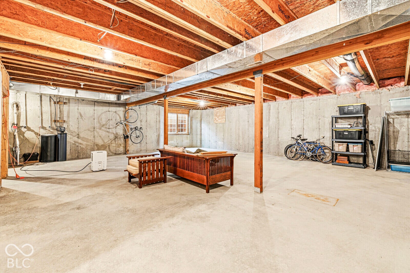 Unfinished basement featuring exposed wood joists, concrete foundation walls, concrete flooring, and an egress window