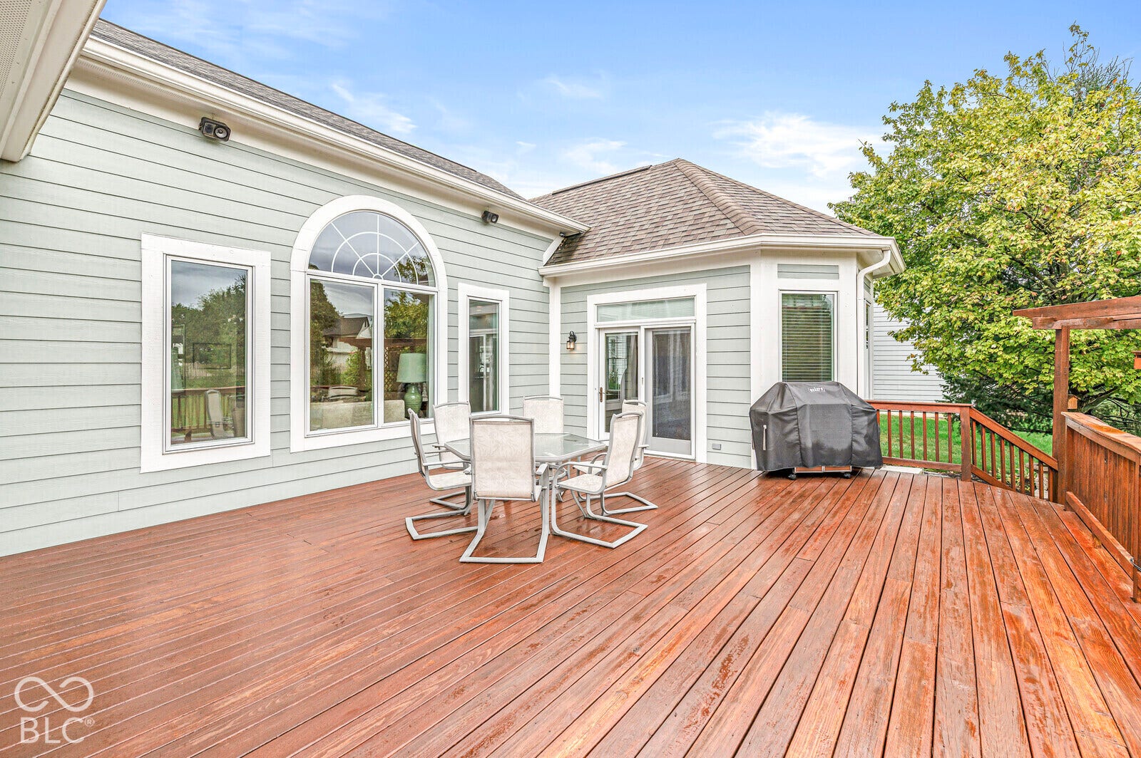 Expansive wood-finish deck with a wood railing, siding exterior, and multiple windows including an arched transom window