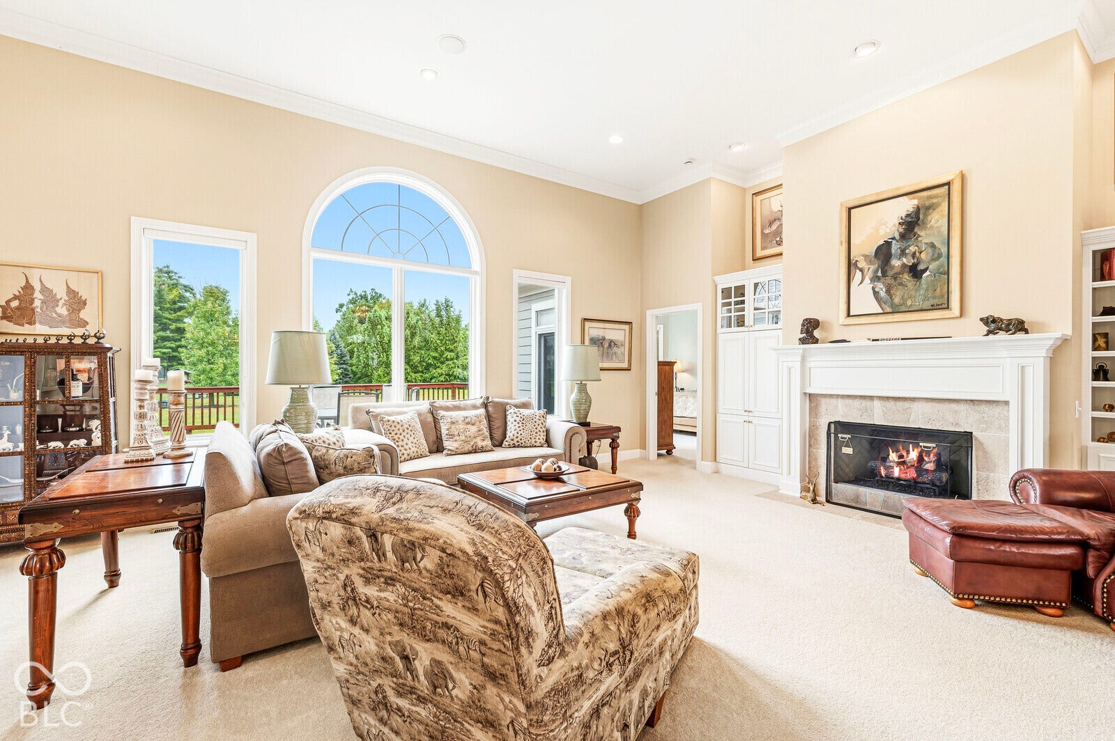 Expansive living area featuring vaulted ceilings, a fireplace with a stone surround, built-in shelving, and large windows with an arched transom