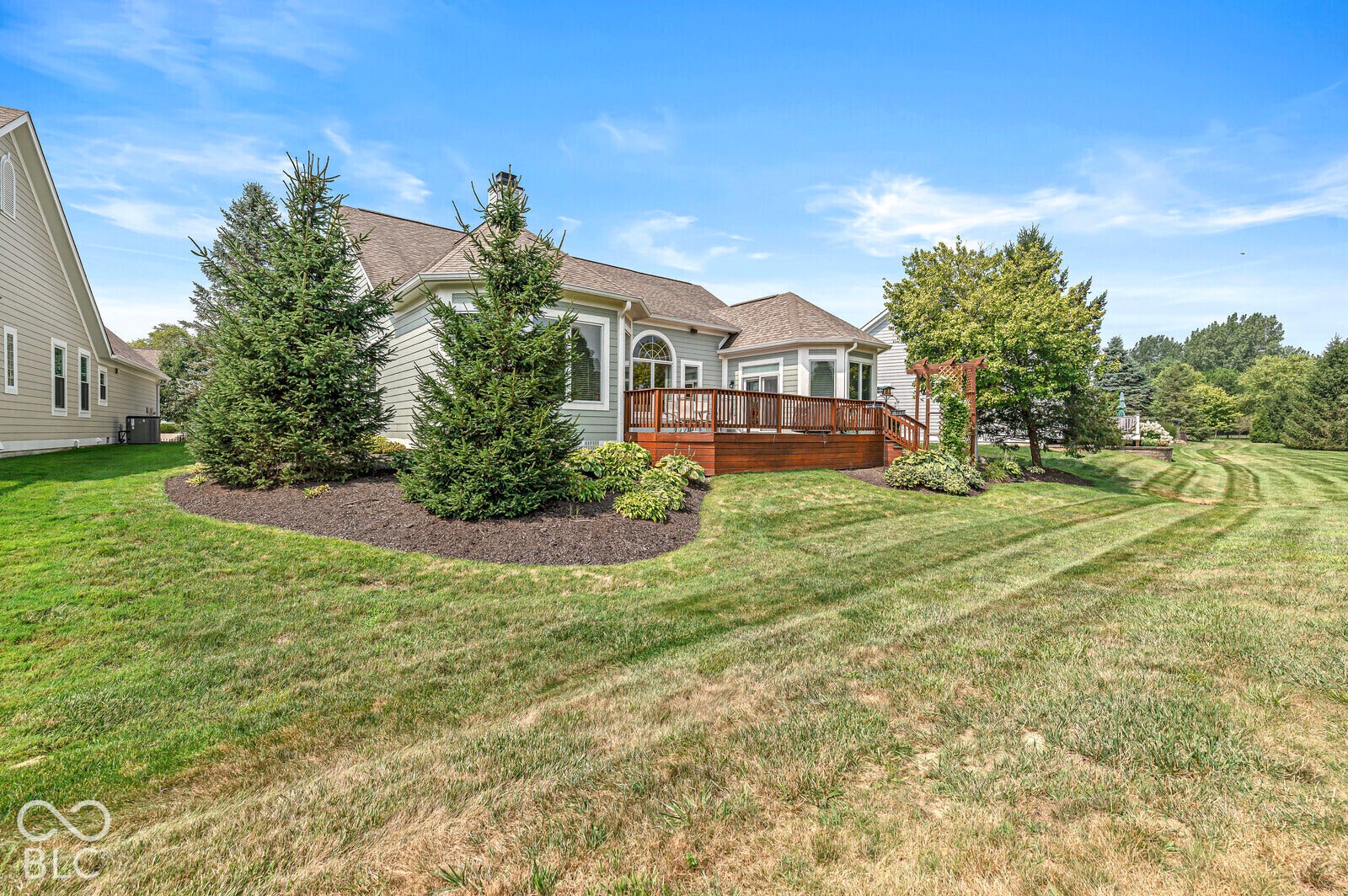 Expansive green lawn with a composite deck, mature trees, and landscaping