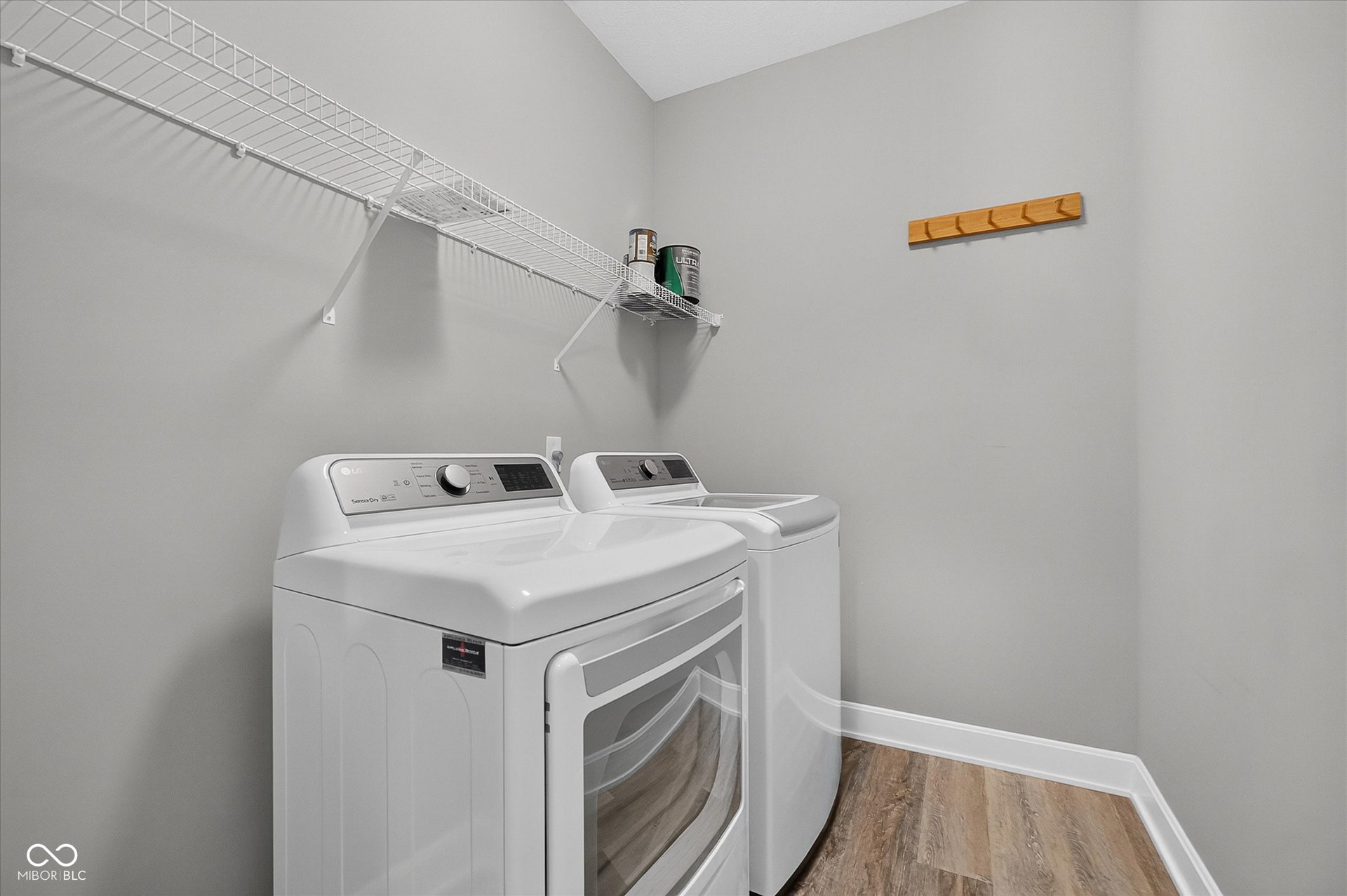Laundry area featuring wood-finish flooring, white wire shelving, and a wall-mounted wooden coat rack