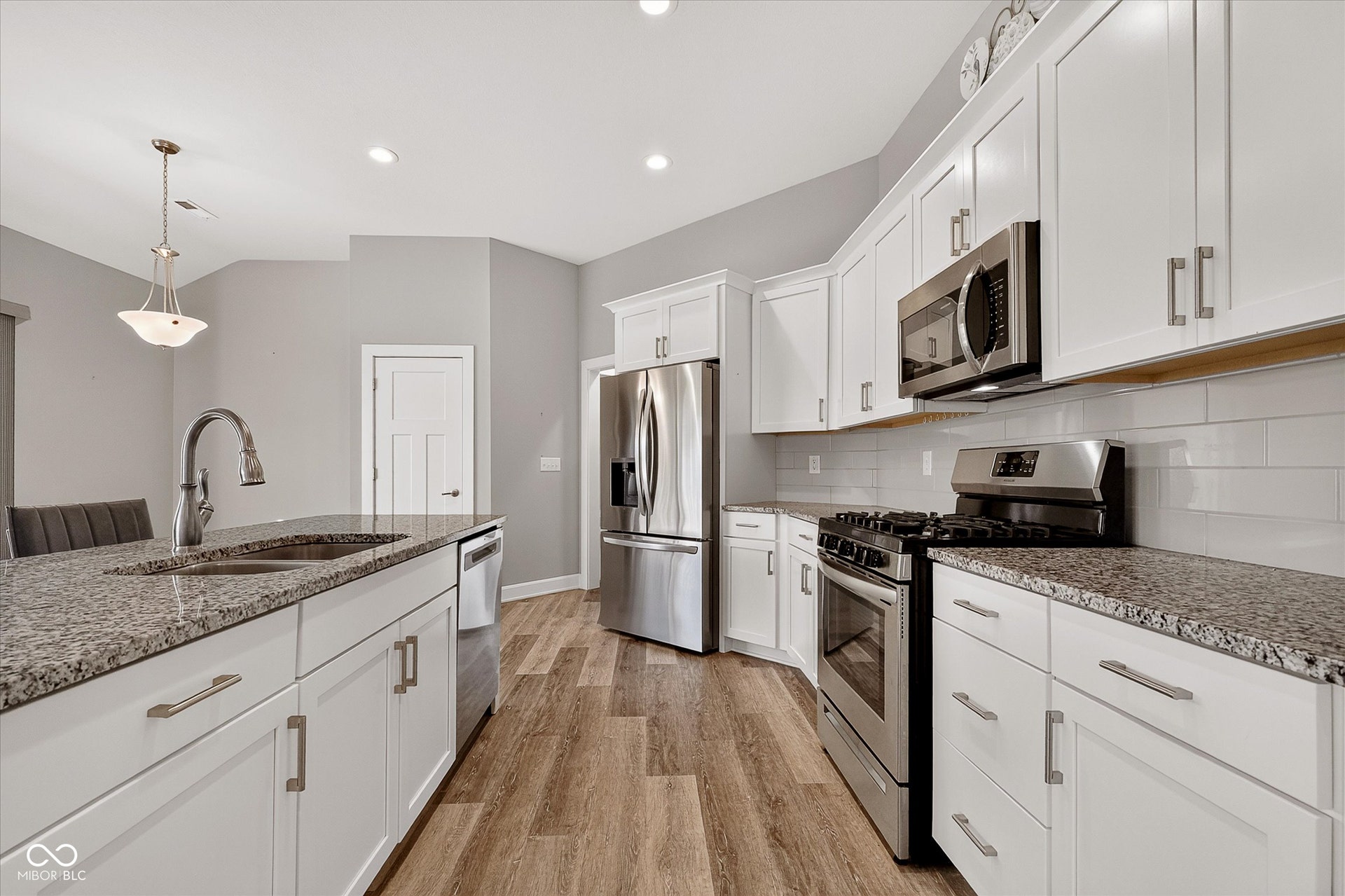 Kitchen featuring white cabinetry, stone countertops, stainless steel appliances, wood-finish flooring, and a subway tile backsplash